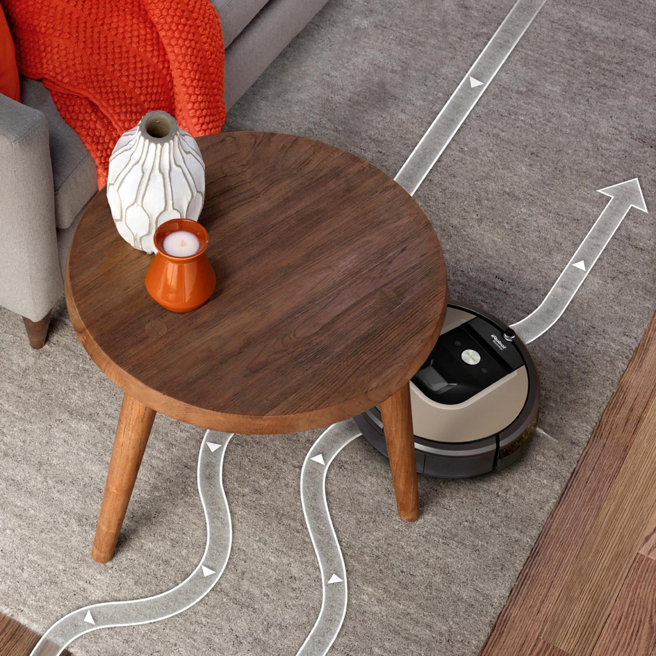 Odkurzacz automatyczny czyści dywan obok drewnianego stolika z dekoracjami. Strzałki pokazują ścieżkę.