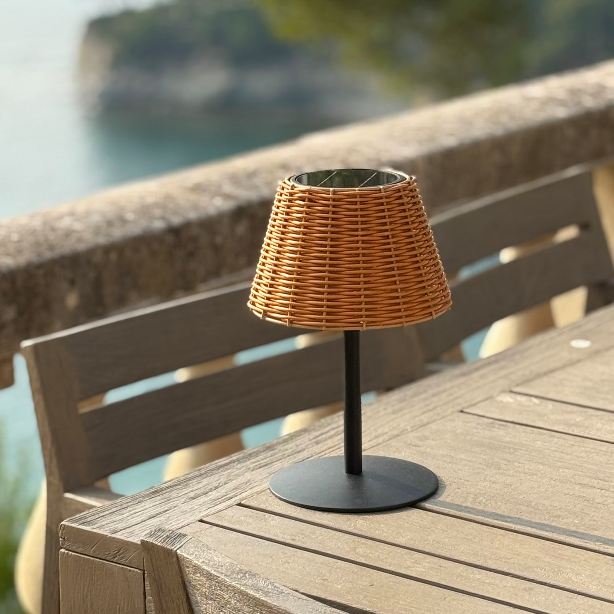 Braune Weidenlampe auf einem Holztisch mit Meerblick im Hintergrund.