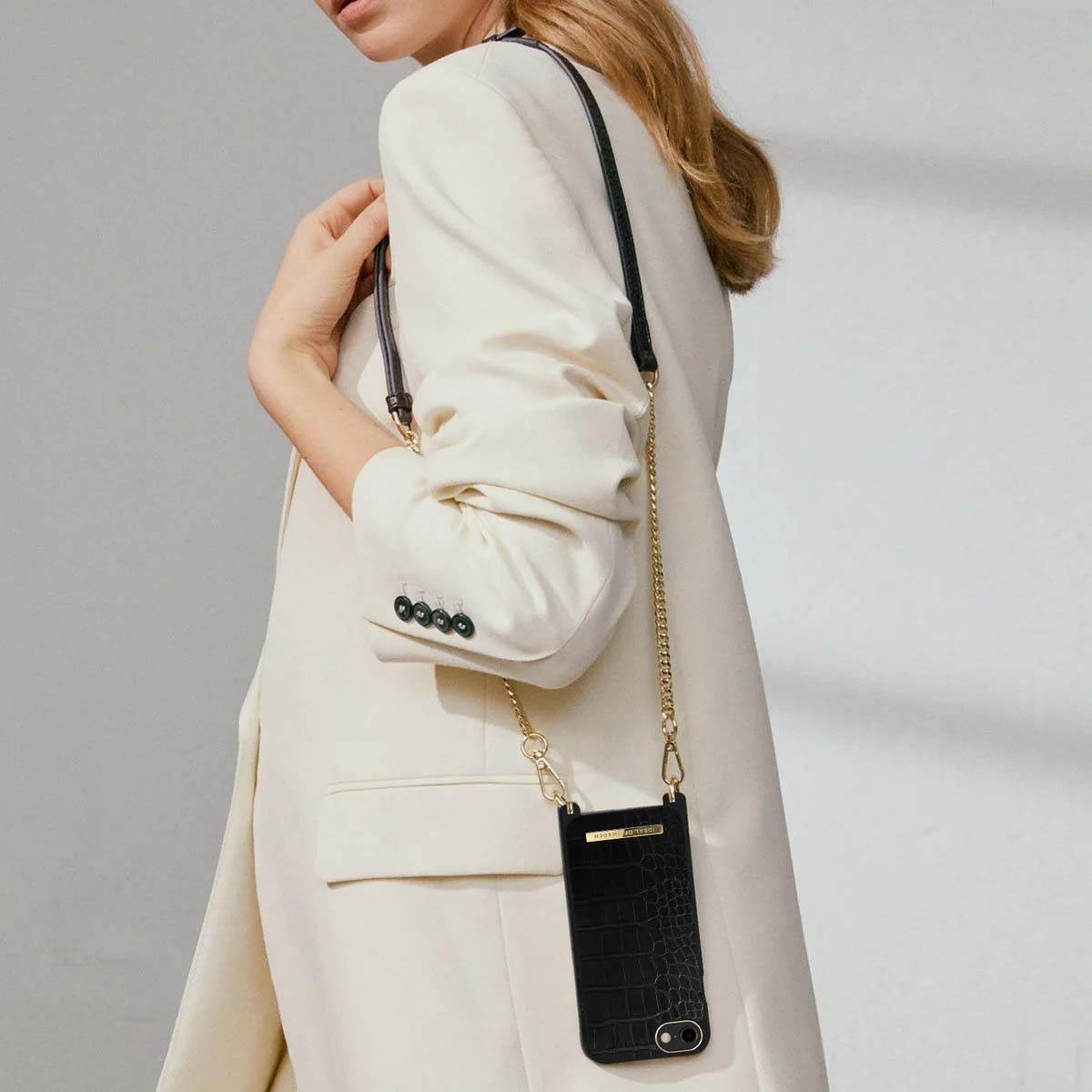 Donna in blazer color crema indossa custodia nera coccodrillo con catena oro.