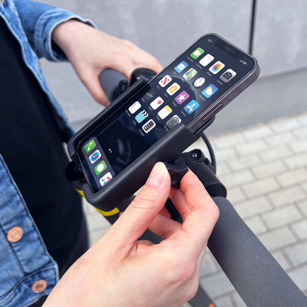 Eine Person befestigt ein Smartphone in einer Halterung an einem Rollergriff.