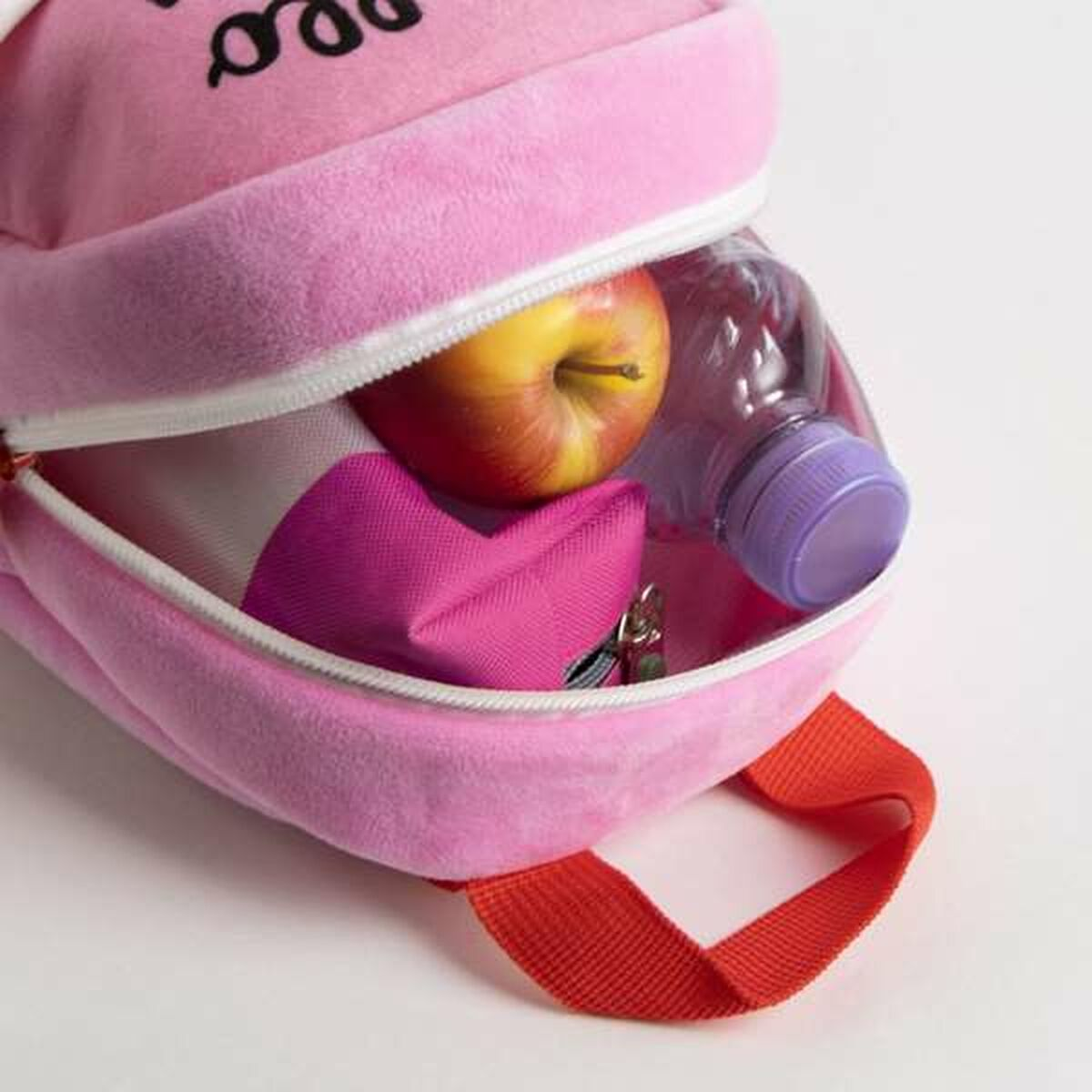 Uno zaino rosa con cerniera. All'interno ci sono una mela, una bottiglia d'acqua e un astuccio rosa.