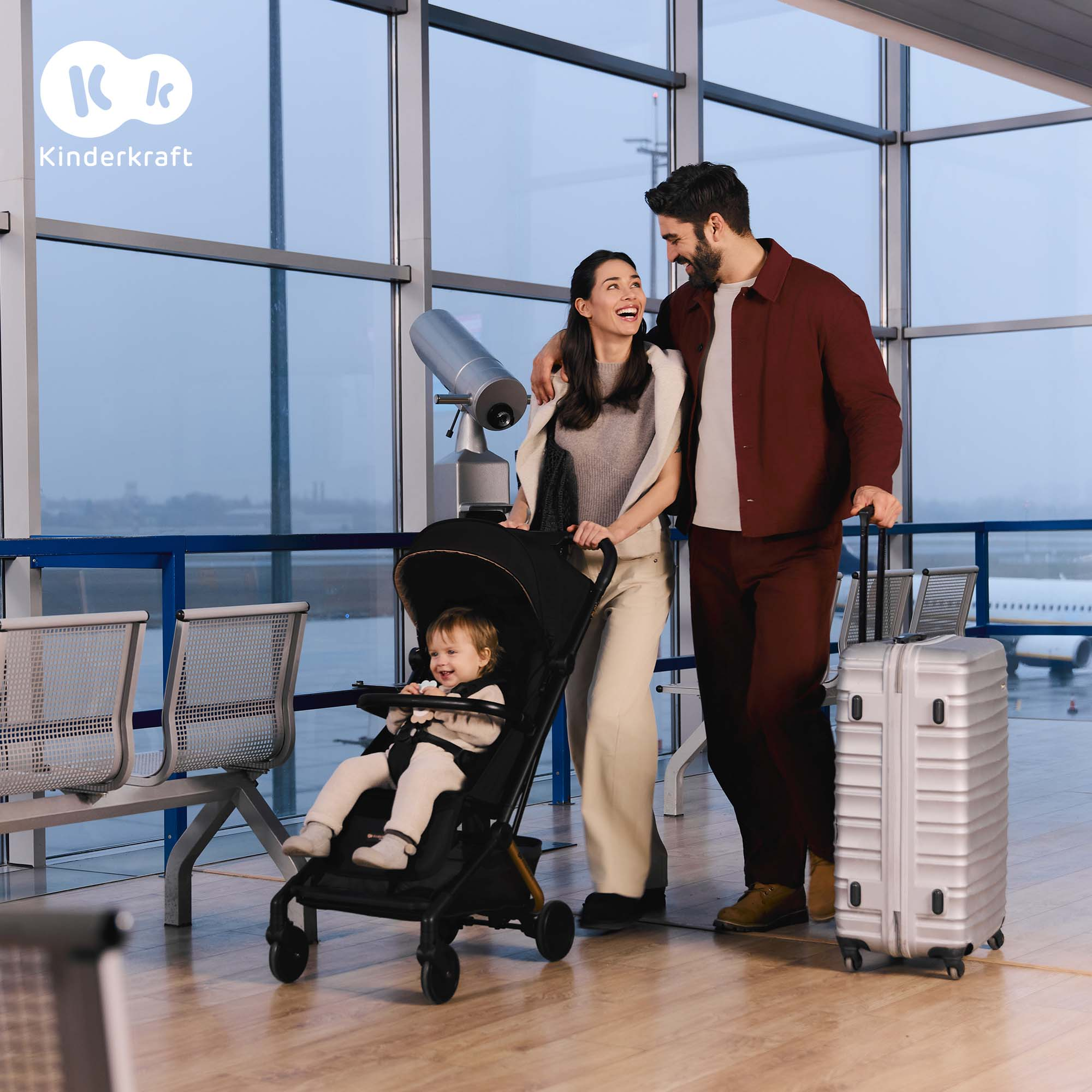 Familie am Flughafen mit Kinderwagen und Koffer, Blick durch Fenster.
