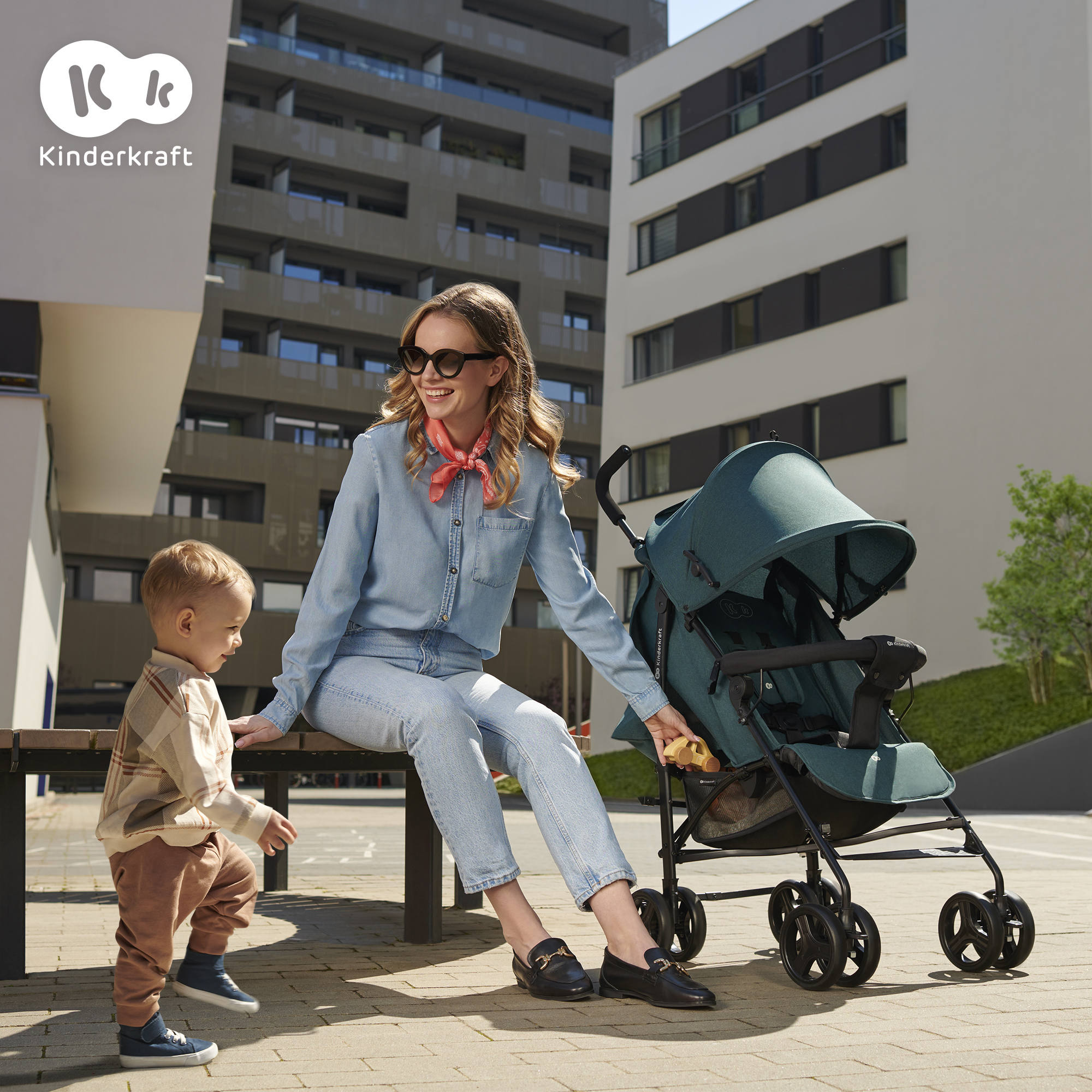 Eine Frau und ein Kleinkind sitzen auf einer Bank neben einem Kinderwagen im Freien.