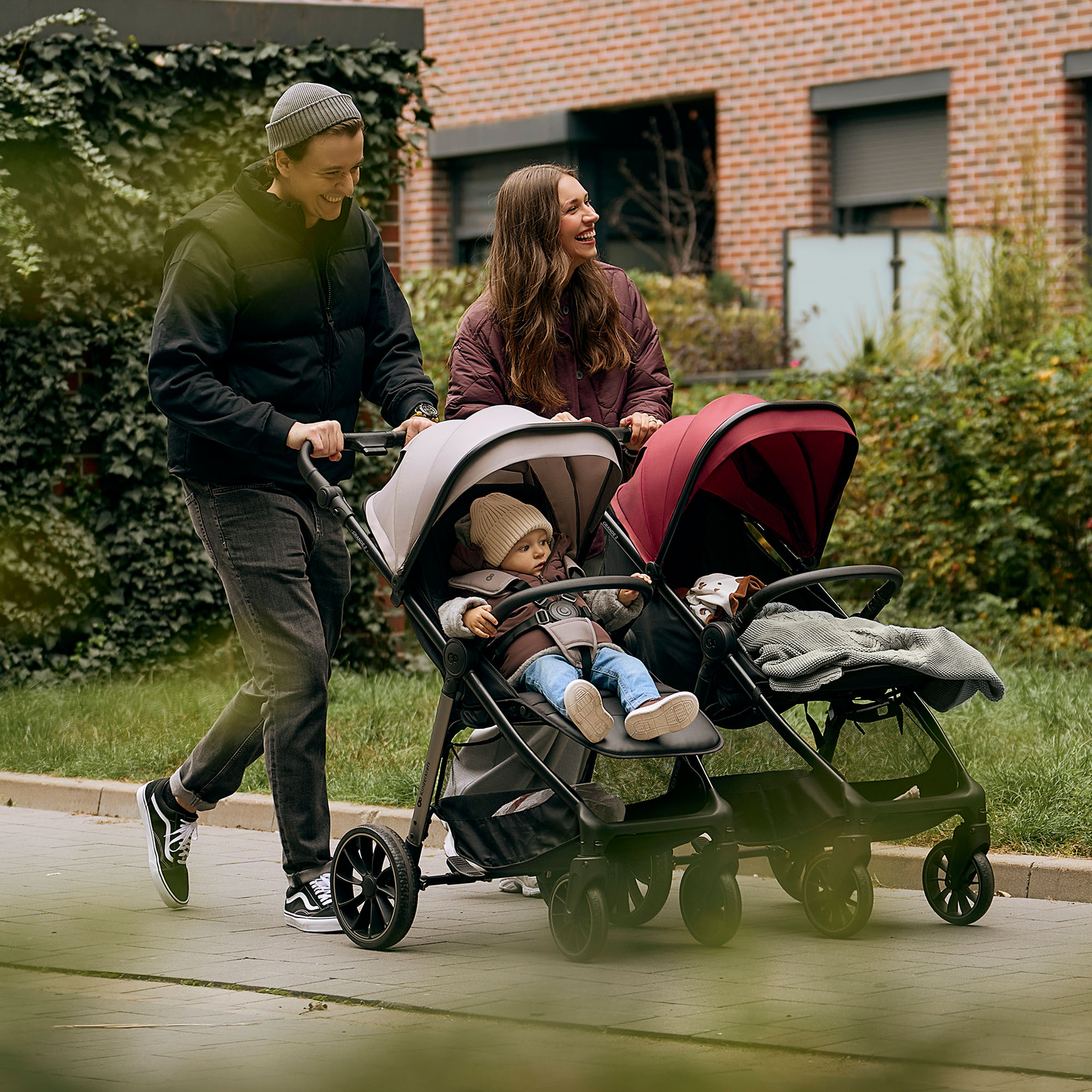 Ein Paar schiebt einen Kinderwagen mit zwei Kindern, draußen