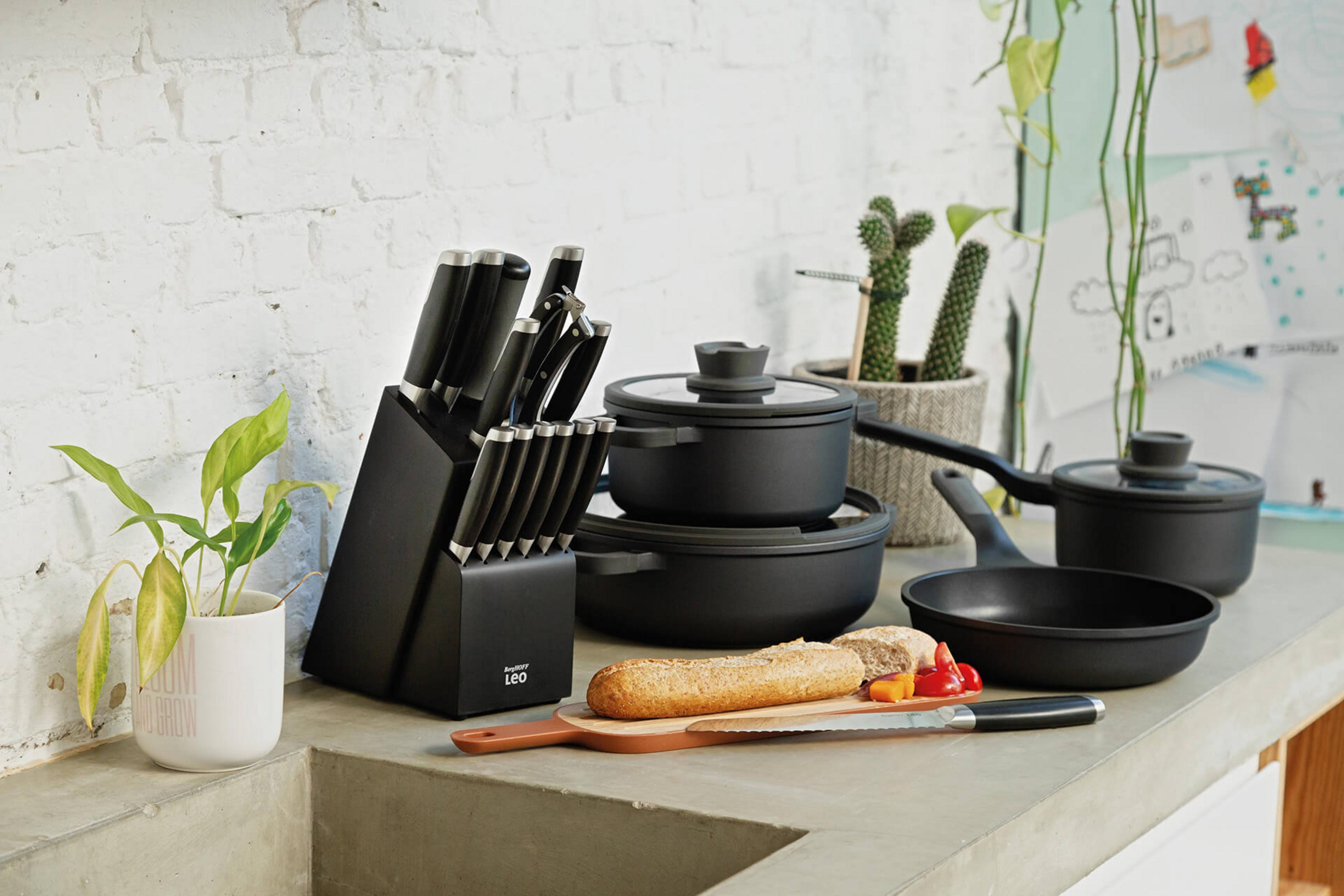 Kitchenware: knife block, pots, pan, bread, and vegetables on a concrete surface.
