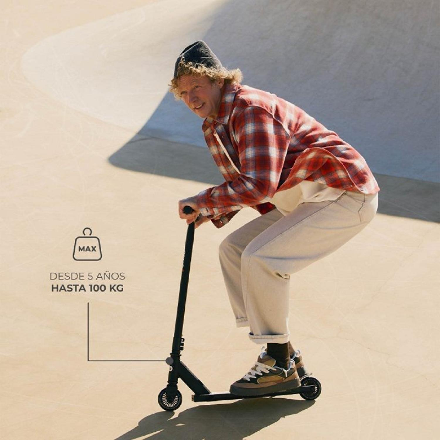 Ein Mann mit Locken und Mütze fährt einen Roller in einem Skatepark.