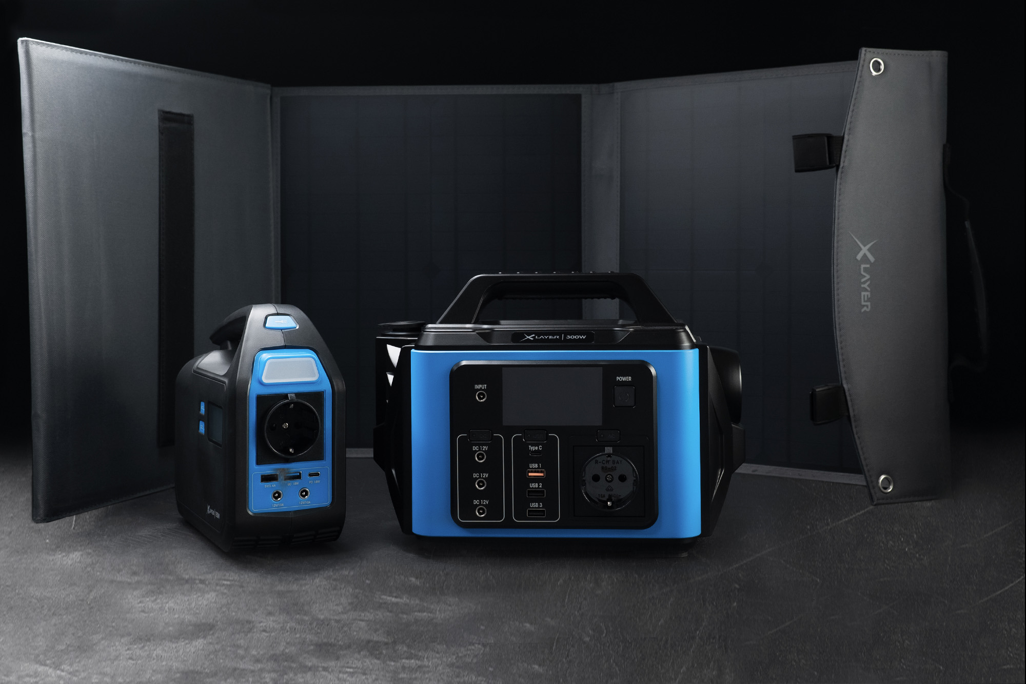 Dwie przenośne elektrownie i składany panel słoneczny na ciemnym tle.