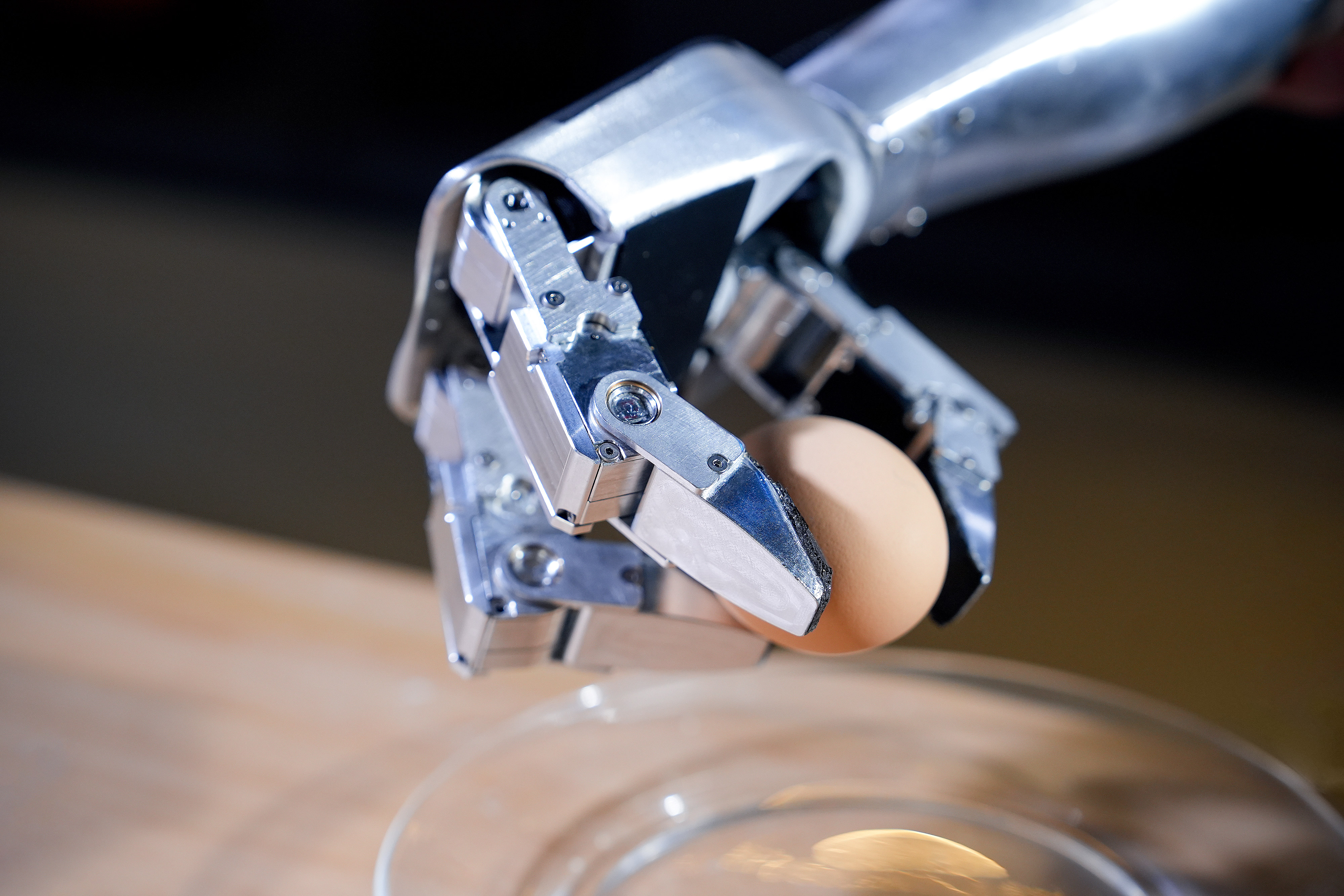 Ein Roboterarm hält ein braunes Ei über einer Glasschale.