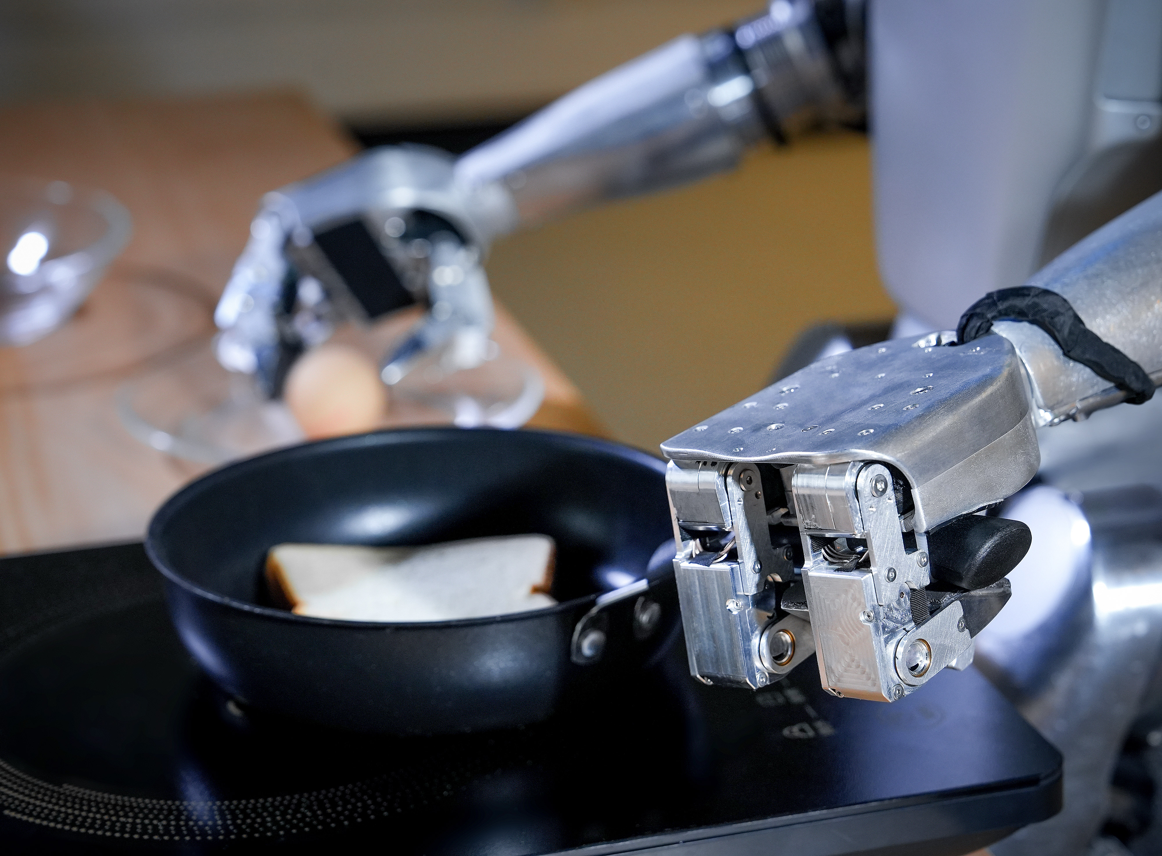 Roboterarm legt Toast in Pfanne mit Ei daneben.