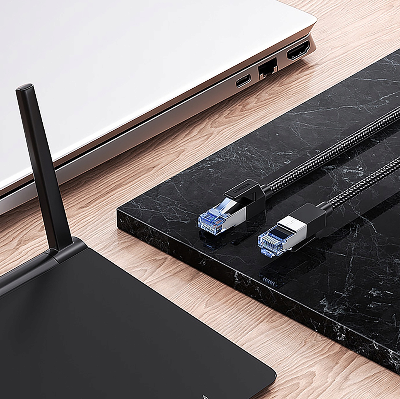 Kable Ethernet z niebieskimi złączami leżą na czarnym marmurze obok laptopa.
