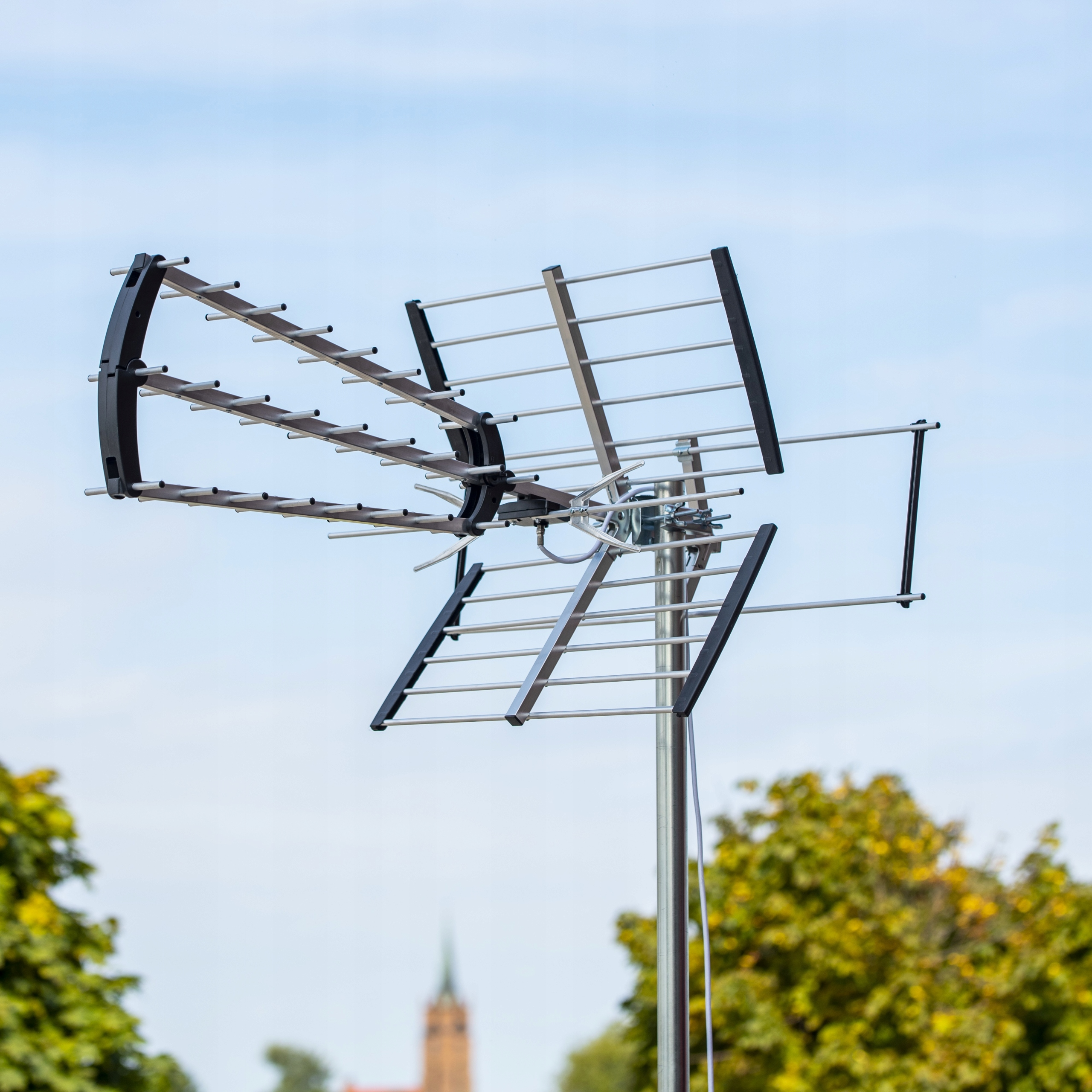 Antena cyfrowa z wieloma prętami na tle błękitnego nieba z drzewami.