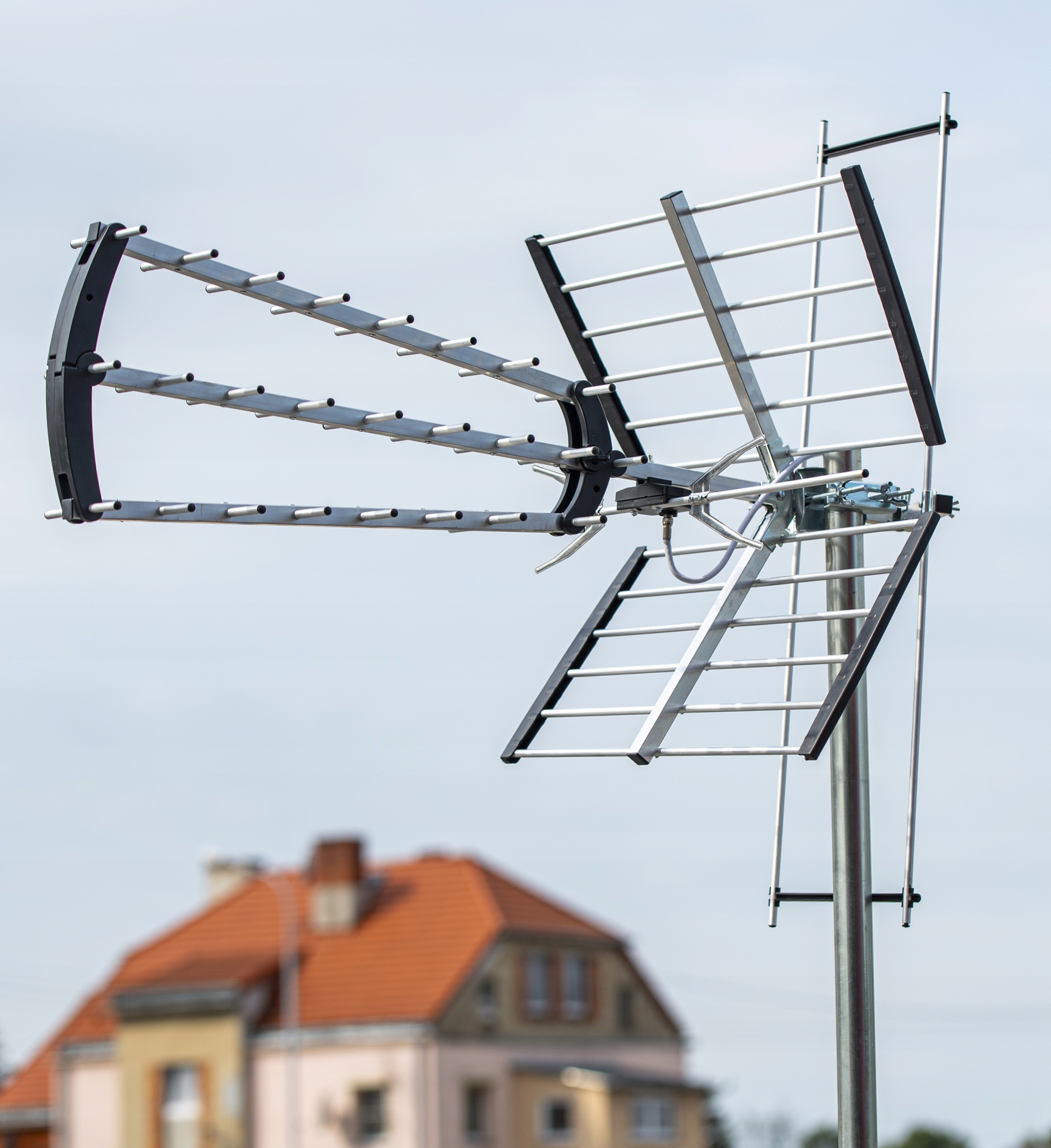 Srebrno-czarna antena zamontowana na słupie, z domem w tle.