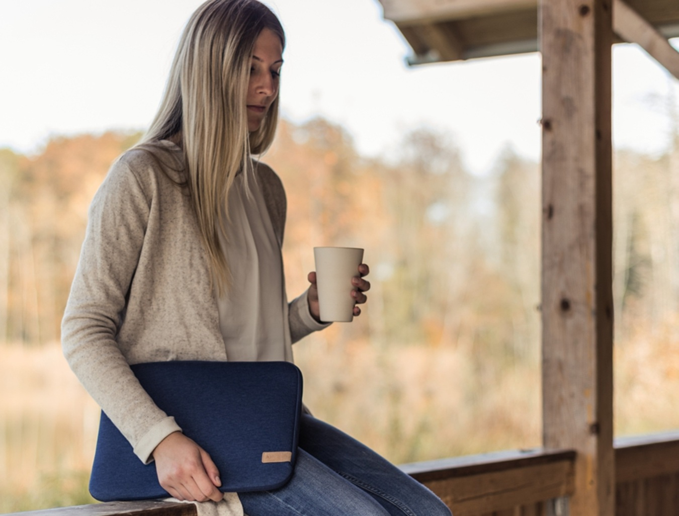 Kobieta z torbą na laptopa i kubkiem siedzi na zewnątrz.