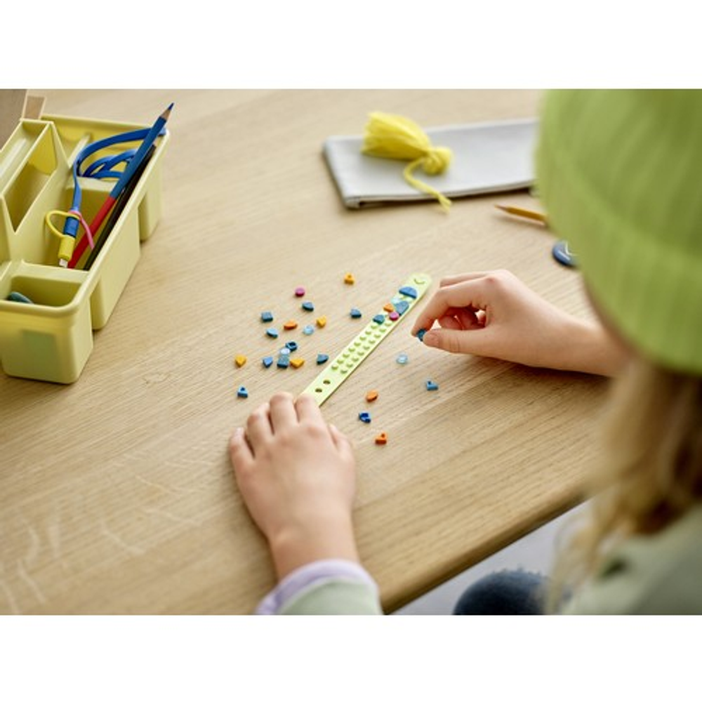 Mani di bambino assemblano braccialetto colorato con tessere piccole su tavolo legno.