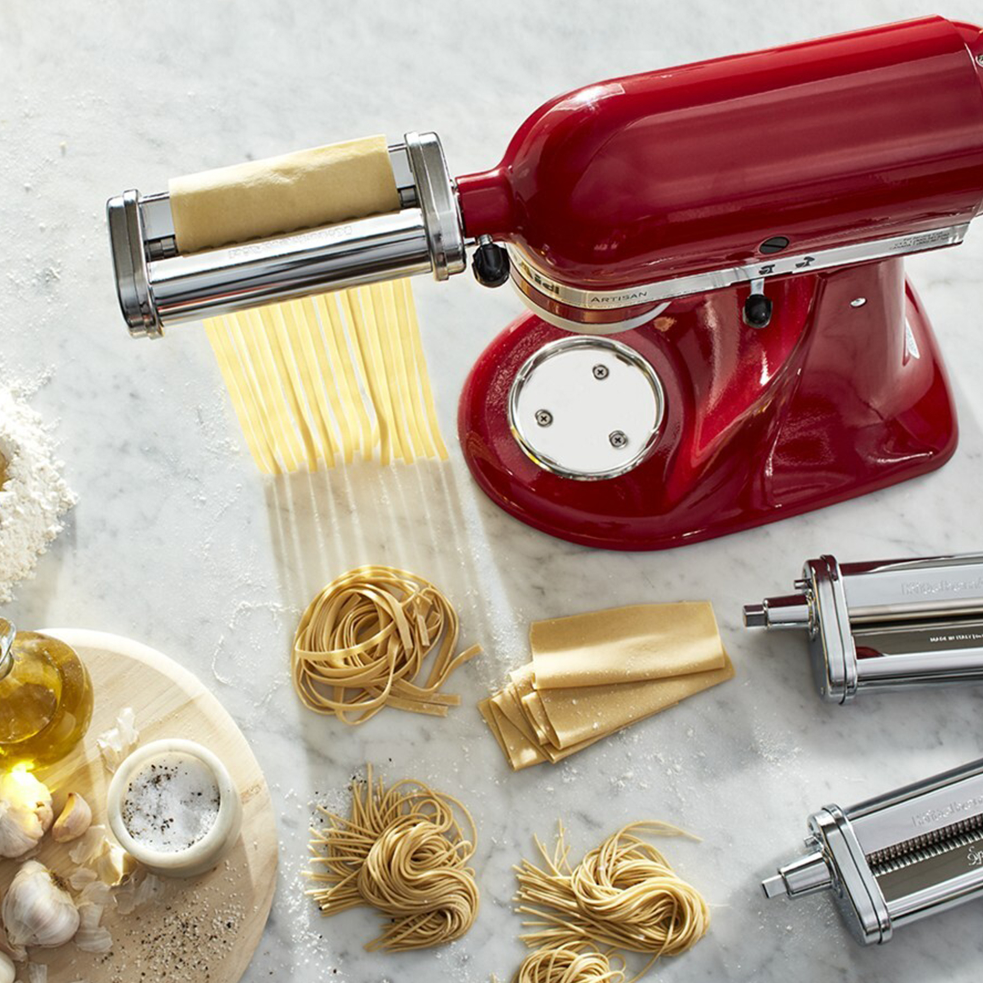Robot pâtissier rouge faisant des pâtes. Des ingrédients comme de l'huile, de l'ail et du sel sont visibles.