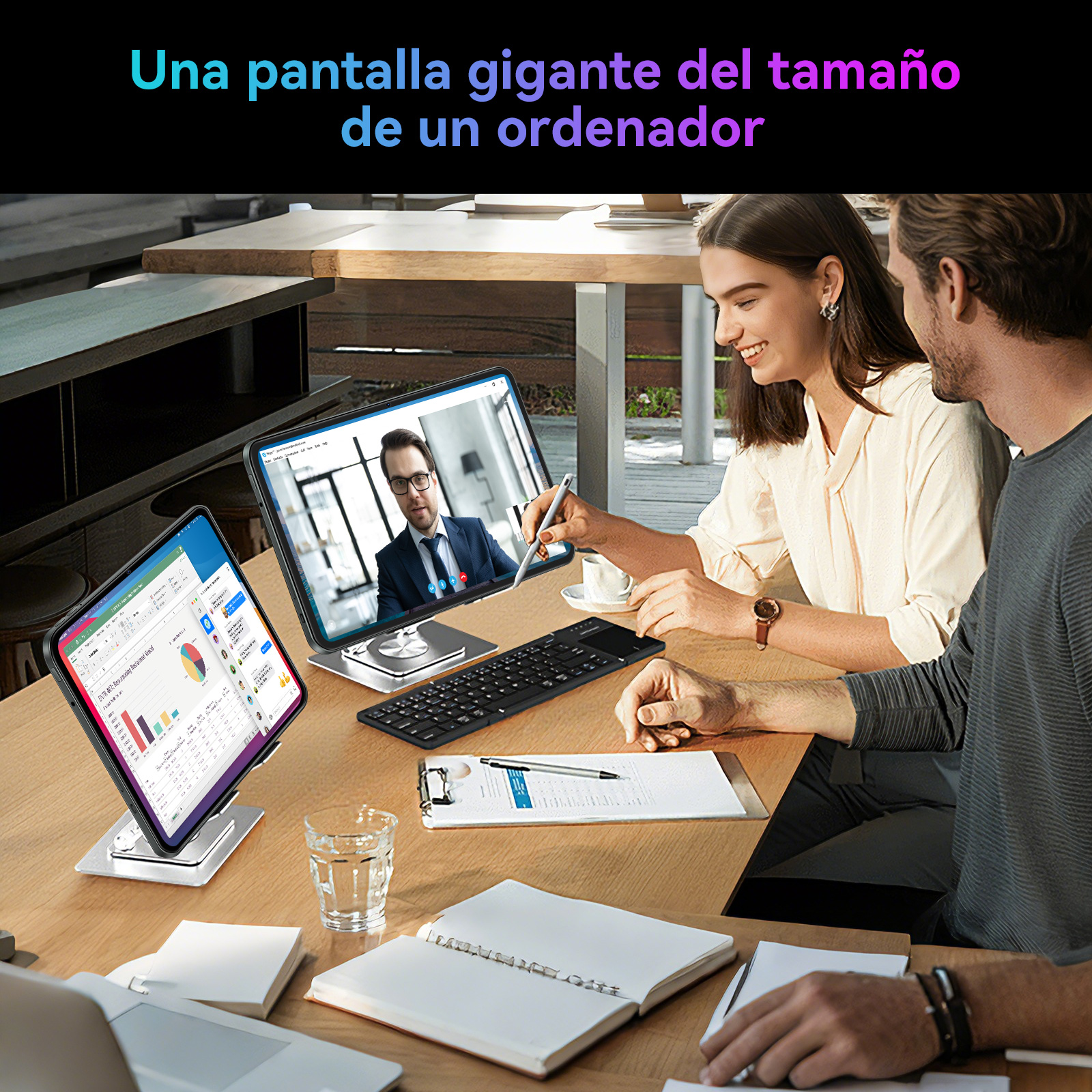 Due persone lavorano a un tavolo con laptop e tablet. Sullo sfondo si vede un uomo.
