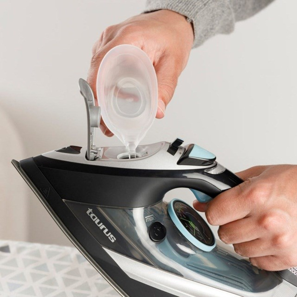 Ręka wlewa wodę z przezroczystego pojemnika do żelazka. Czarne i srebrne żelazko.