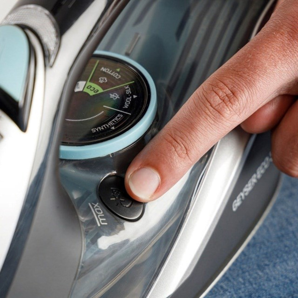 Palec naciska przycisk na żelazku z ustawieniami temperatury.