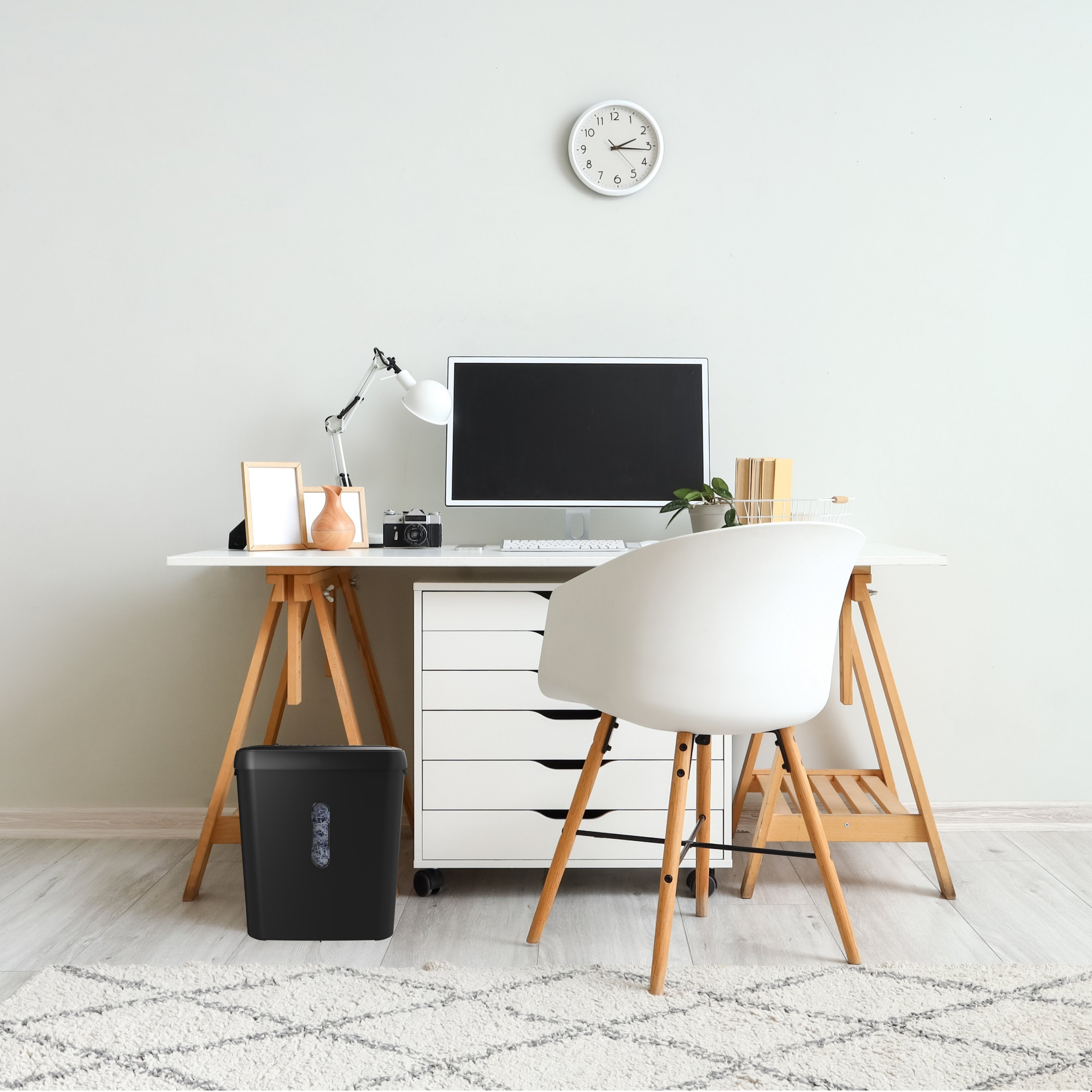 A desk with a computer, lamp, camera, and a clock on the wall.