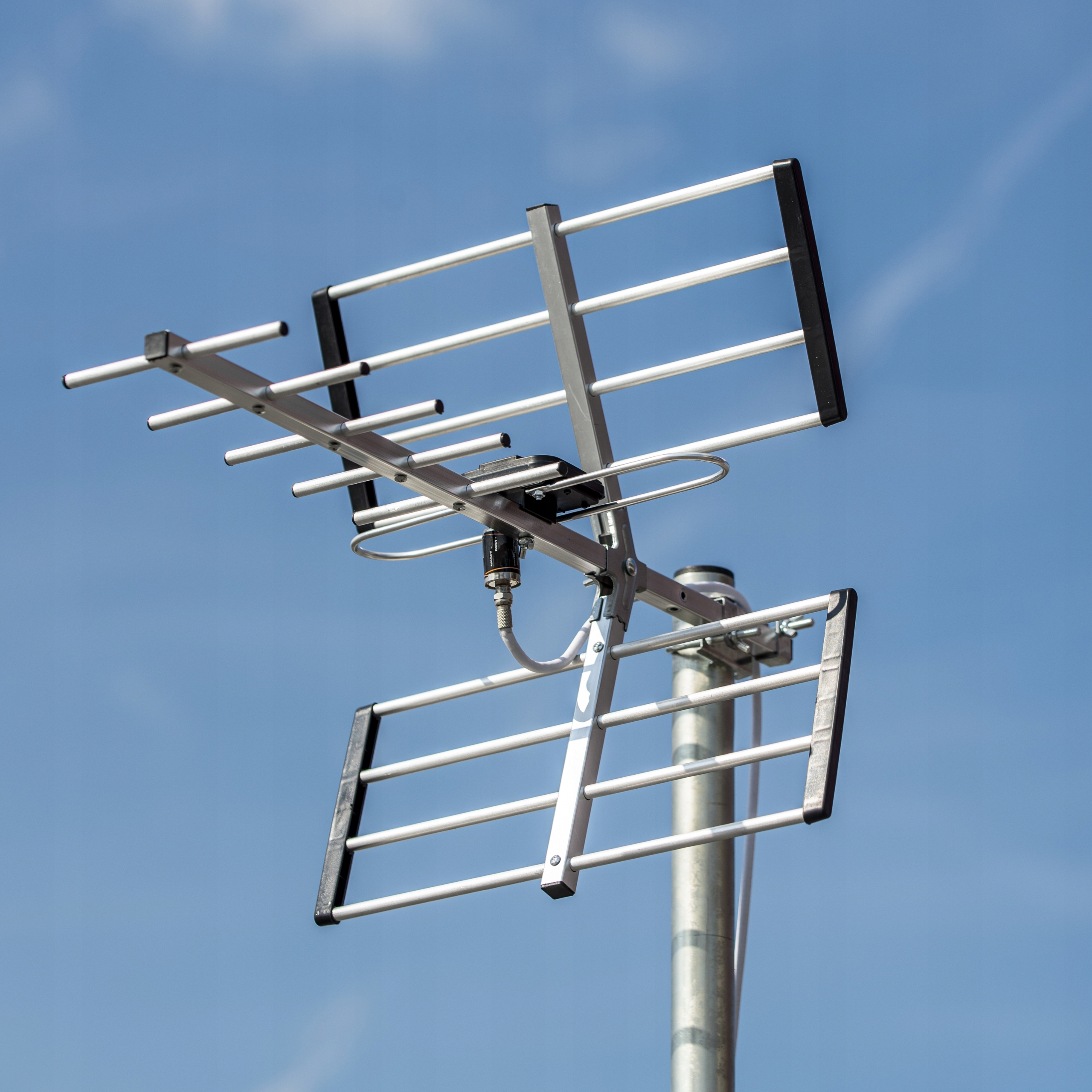 Metalowa antena telewizyjna z wieloma prętami na tle niebieskiego nieba.