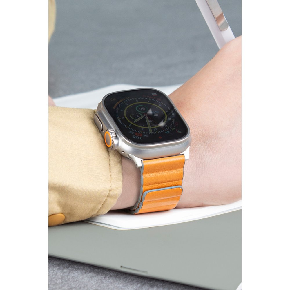 Bir kişinin kolunda, turuncu deri kayışlı gümüş bir Apple Watch var, dijital ekran saati ve pusulayı gösteriyor.