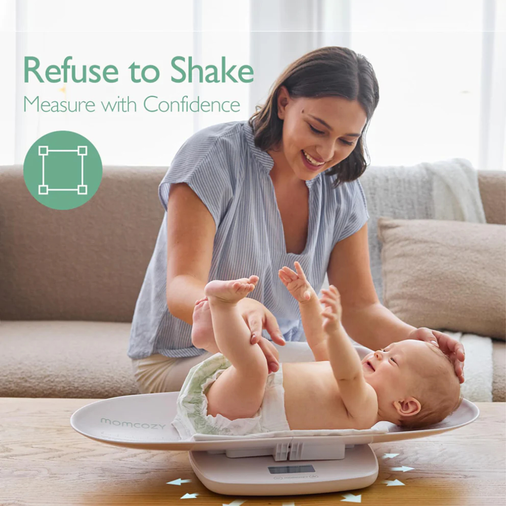 Una donna sorridente guarda un bambino sdraiato su una bilancia bianca per neonati su un tavolo di legno. Testo: Refuse to Shake.