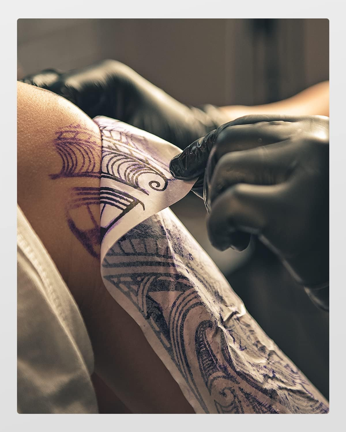 Nahaufnahme eines Arms, auf den von behandschuhten Händen eine Tattoo-Schablone mit komplexen Mustern aufgebracht wird.