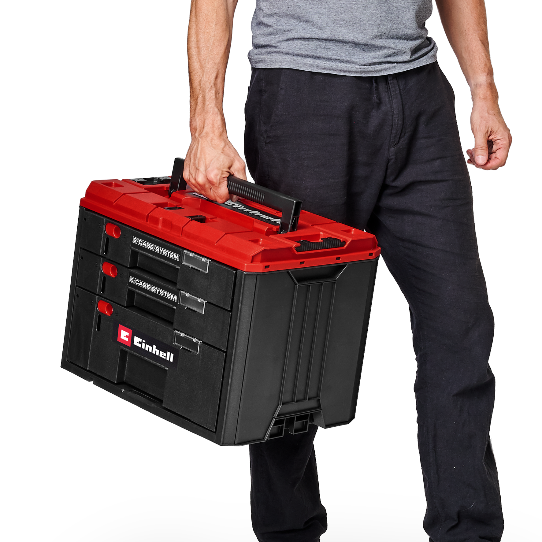 Eine Person in einem grauen Hemd und schwarzer Hose hält eine schwarz-rote Einhell E-Case System Werkzeugkiste.