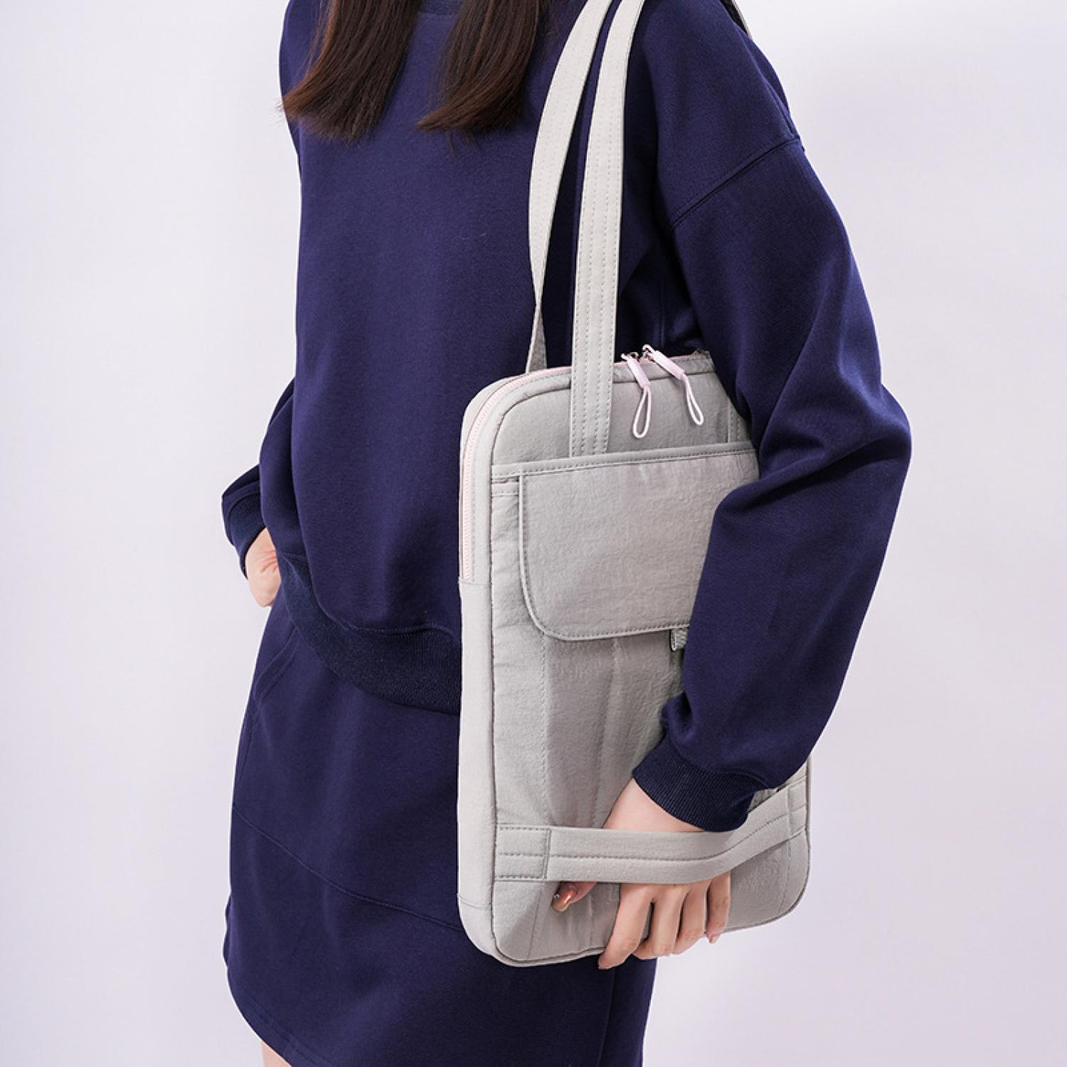 Eine Person in dunkelblauer Kleidung hält eine graue Tasche.