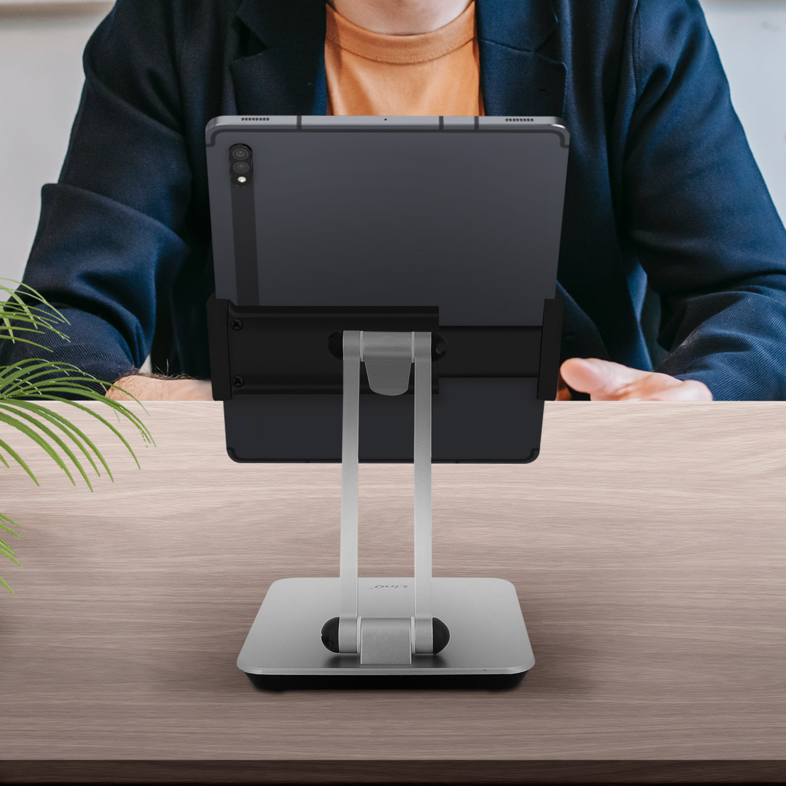 Un tablet su un supporto su una scrivania di legno, persona sullo sfondo.