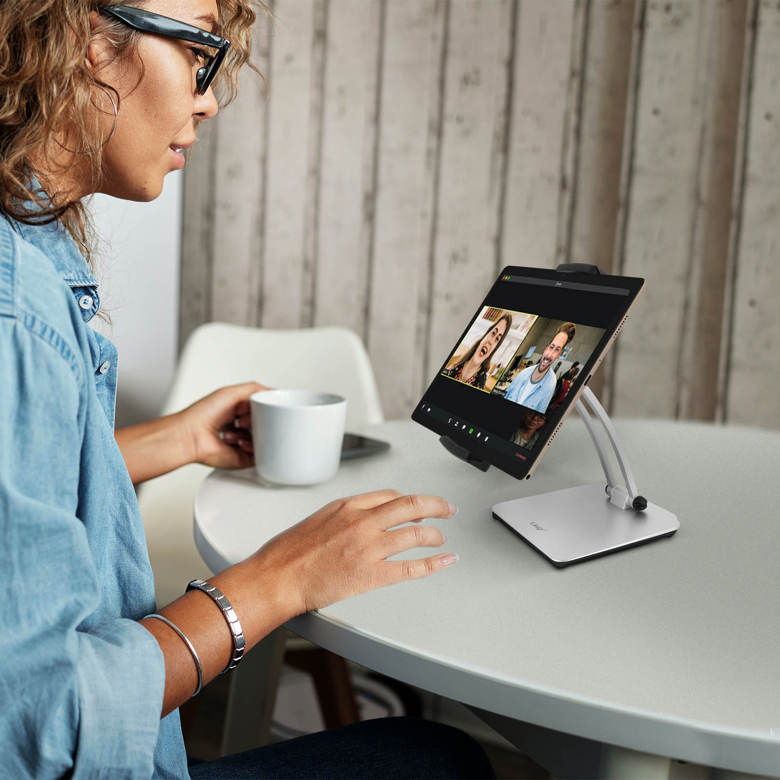 Donna con occhiali tiene tazza, guarda tablet con videochiamata.