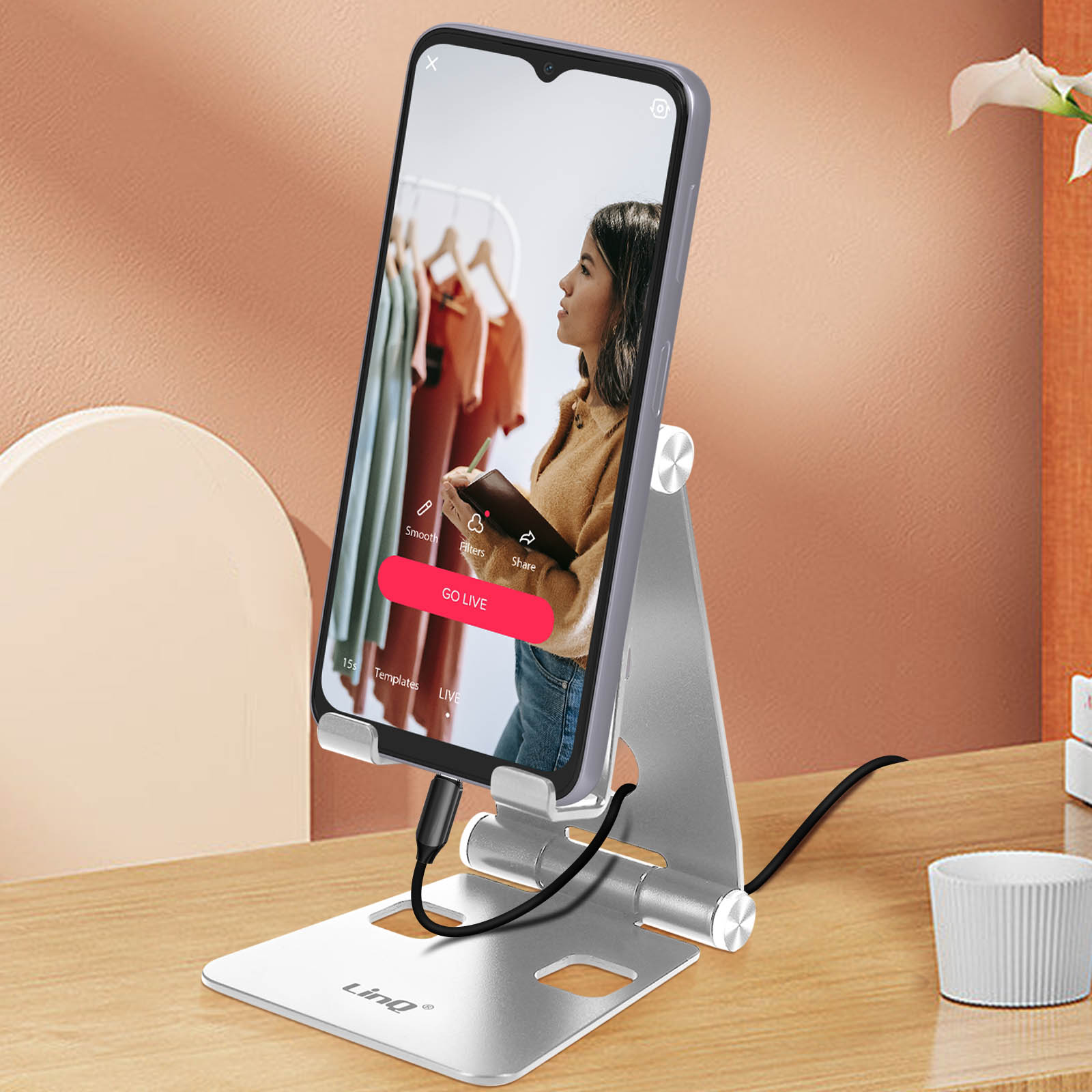 Supporto argento per telefono mostra donna in live streaming vestiti. Setup scrivania.