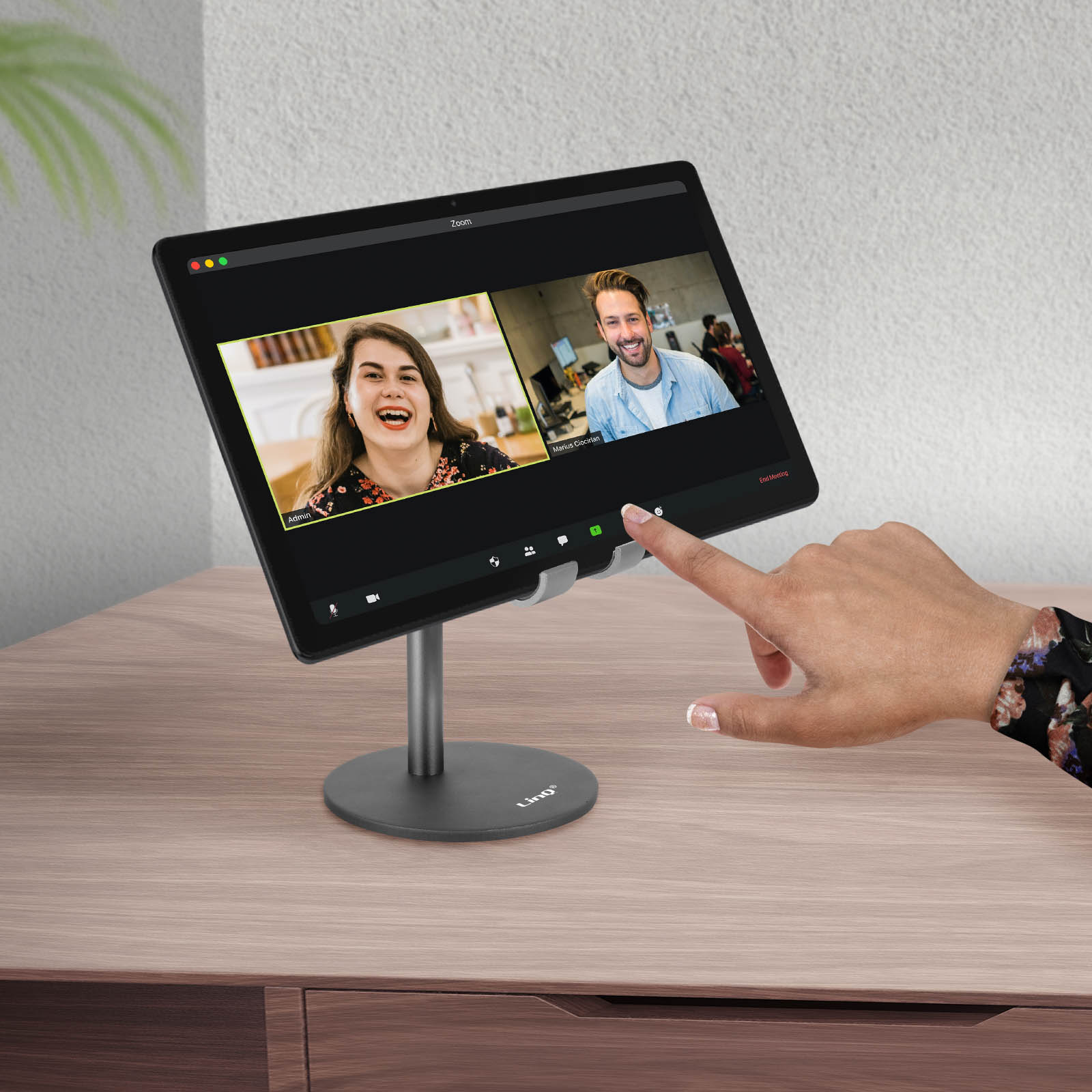 Un tablet mostra una riunione Zoom con due persone. Una mano tocca lo schermo.