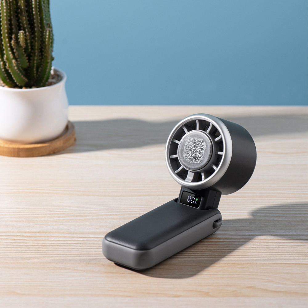 Un ventilador pequeño y oscuro con pantalla LCD sobre una mesa de madera junto a un cactus.