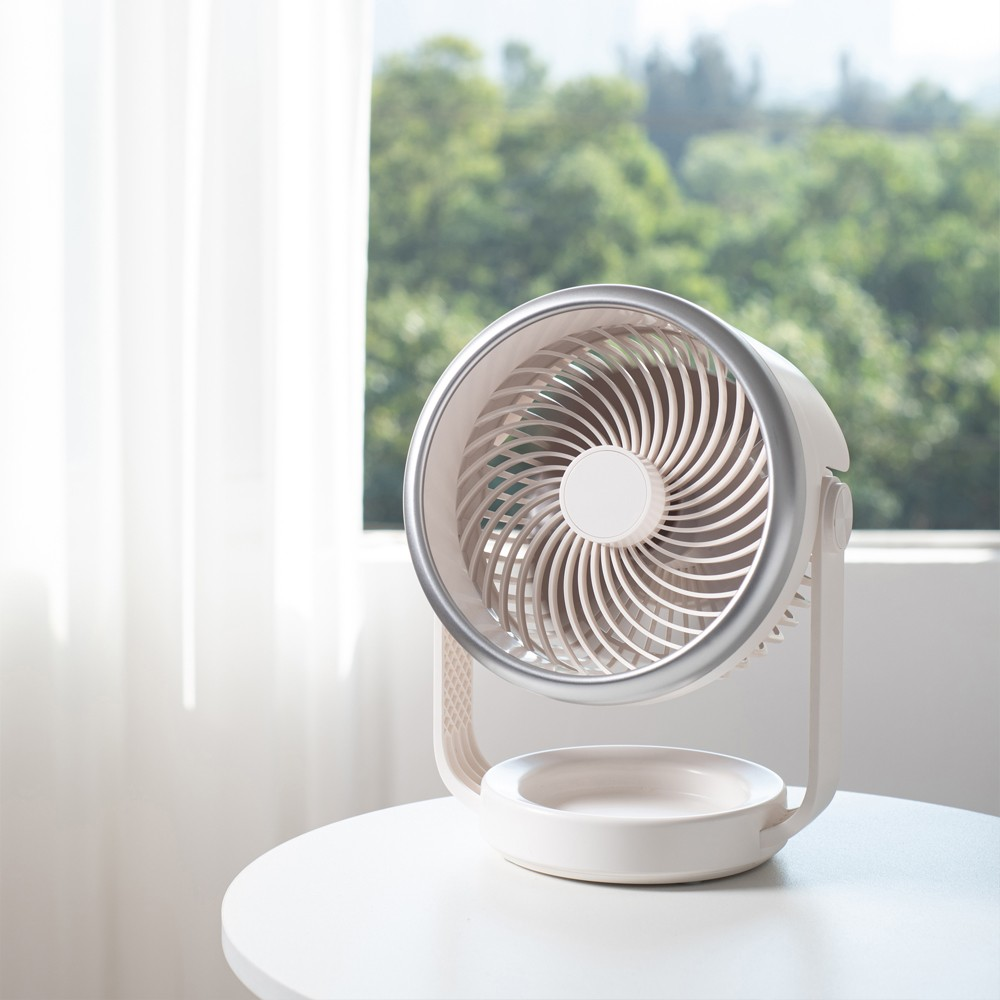 Un ventilador de mesa blanco con borde plateado está sobre una mesa.