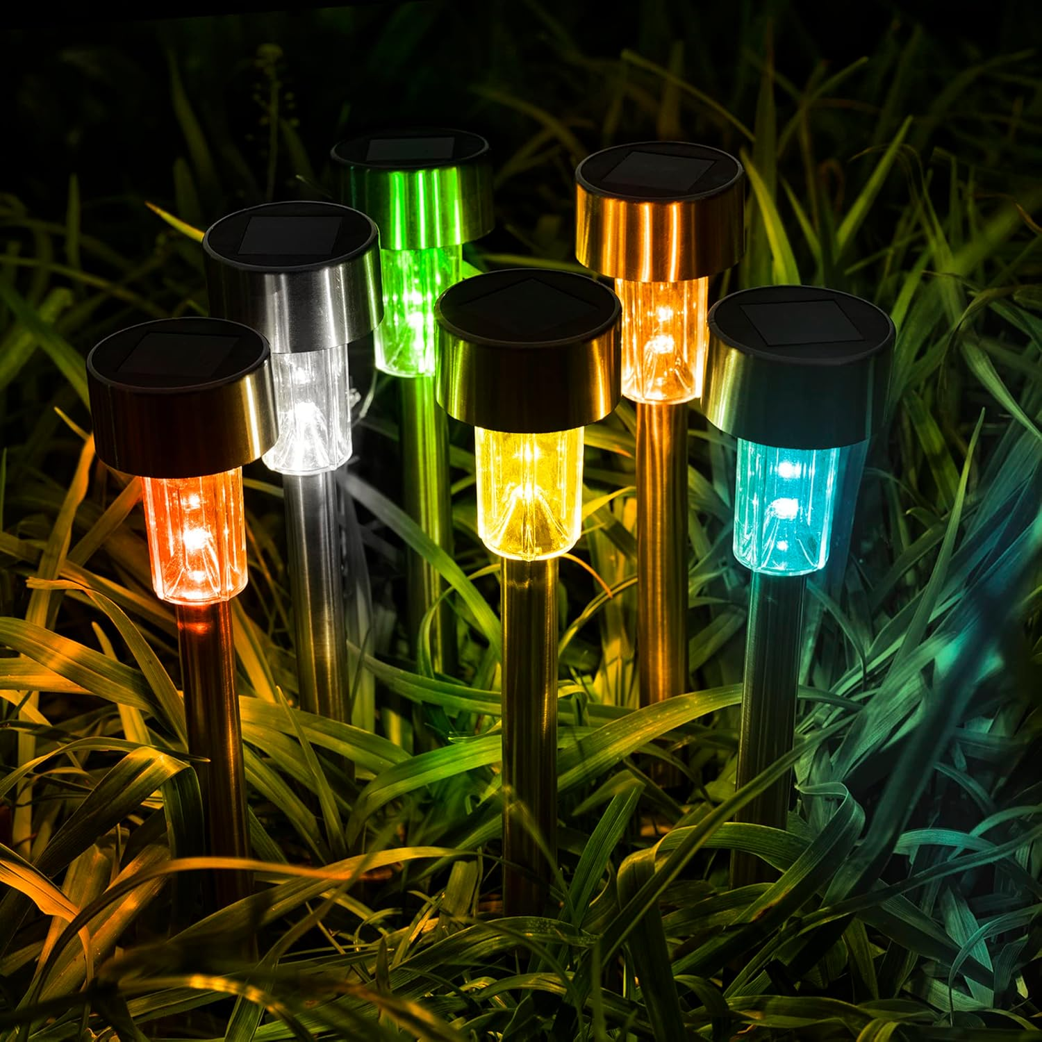 Sechs bunte Solar-Gartenleuchten leuchten nachts orange, weiß, grün, gelb und blau im Gras.
