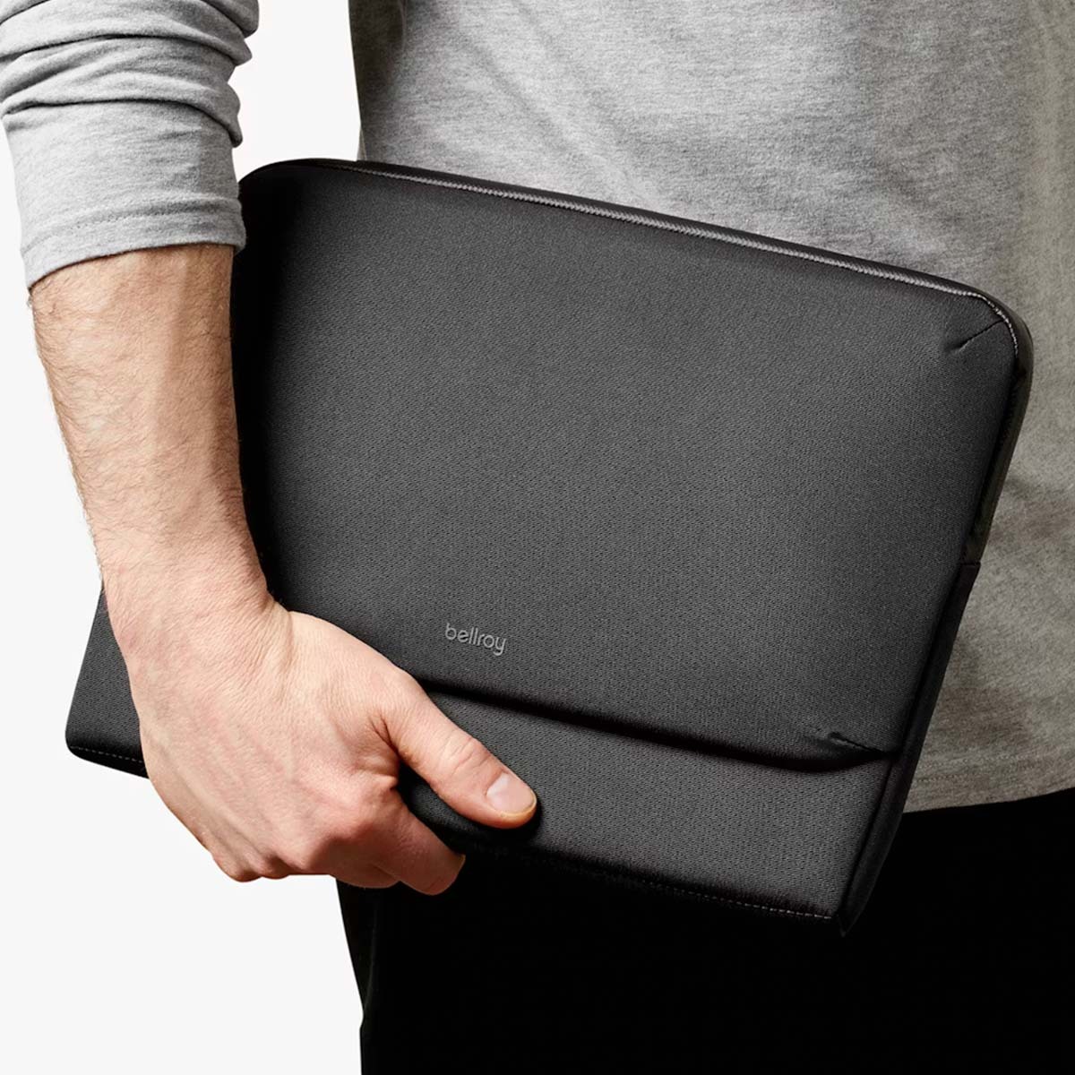 Una mano tiene una custodia nera per laptop con il logo Bellroy.