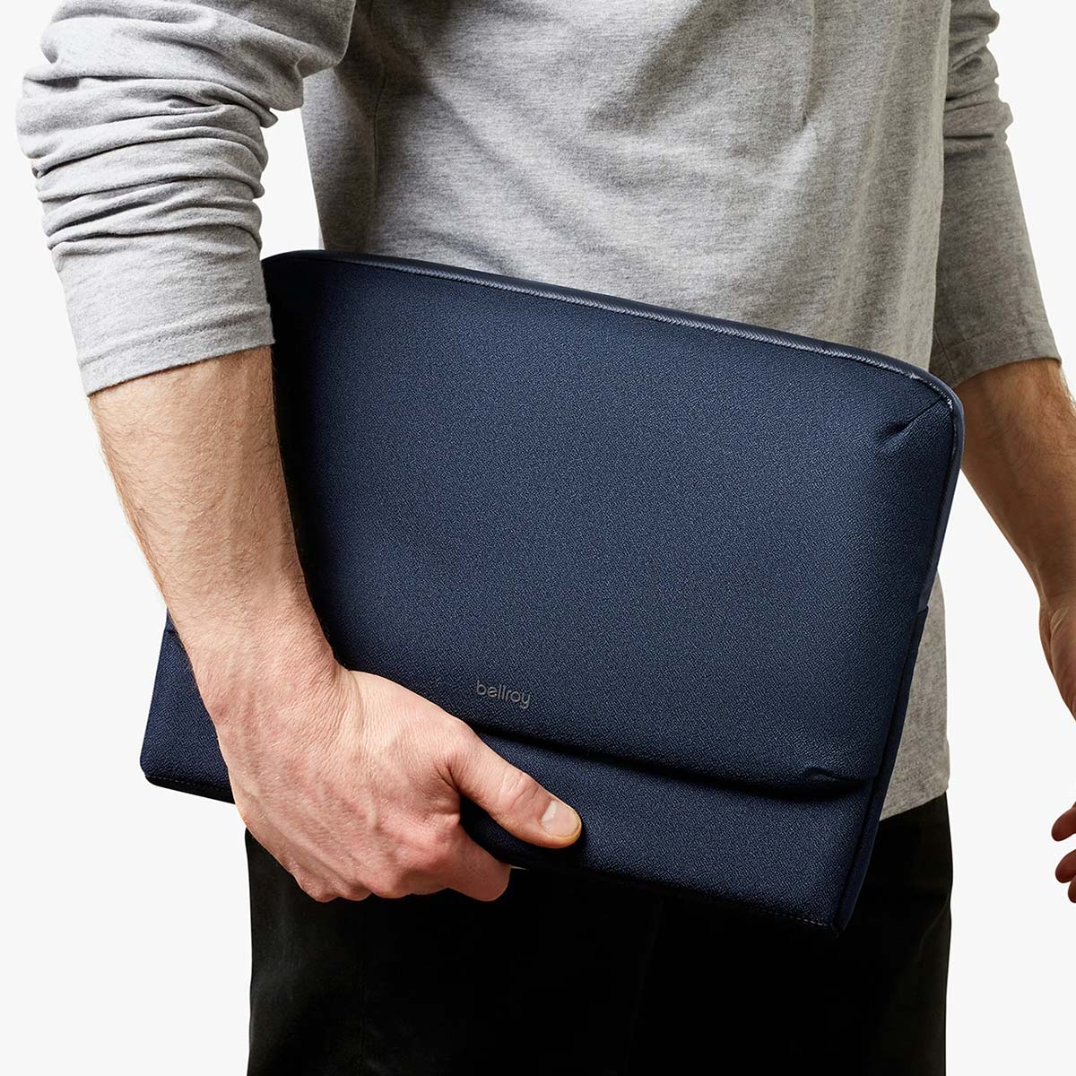 Uomo in maglione grigio tiene una custodia blu scuro per laptop.