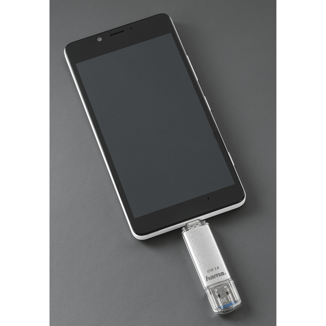 Une clé USB argentée "hama" est branchée sur un smartphone noir.