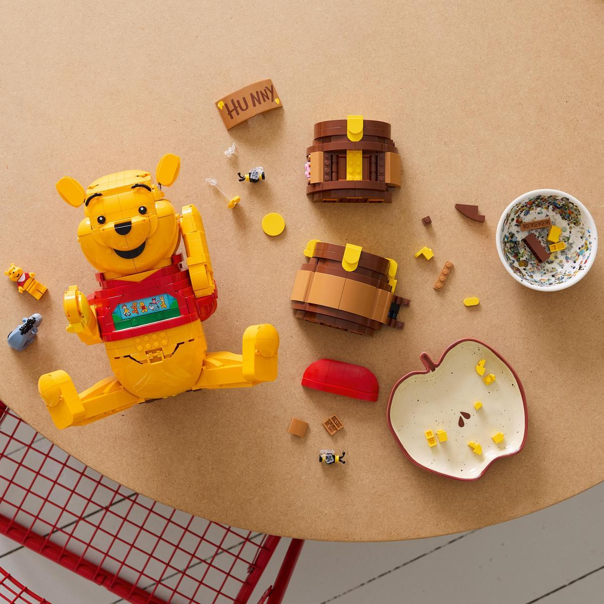 Lego Winnie the Pooh, iki bal fıçısı ve elma tabağının yanında oturuyor.