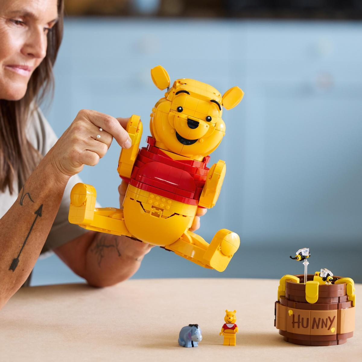 Bir kadın Lego'dan Winnie the Pooh figürü tutuyor. Yakında arılı bir bal kavanozu var.