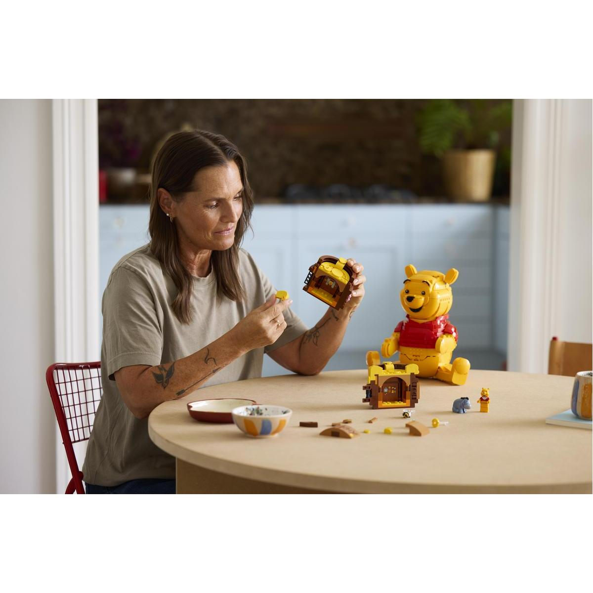 Bir kadın yuvarlak bir masada Winnie the Pooh Lego seti inşa ediyor.
