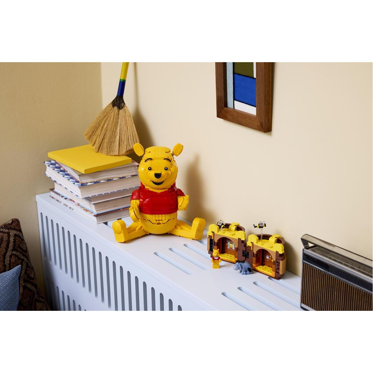 Winnie the Pooh figürü, Lego evlerin ve kitapların yanında oturuyor. Arkada süpürge.