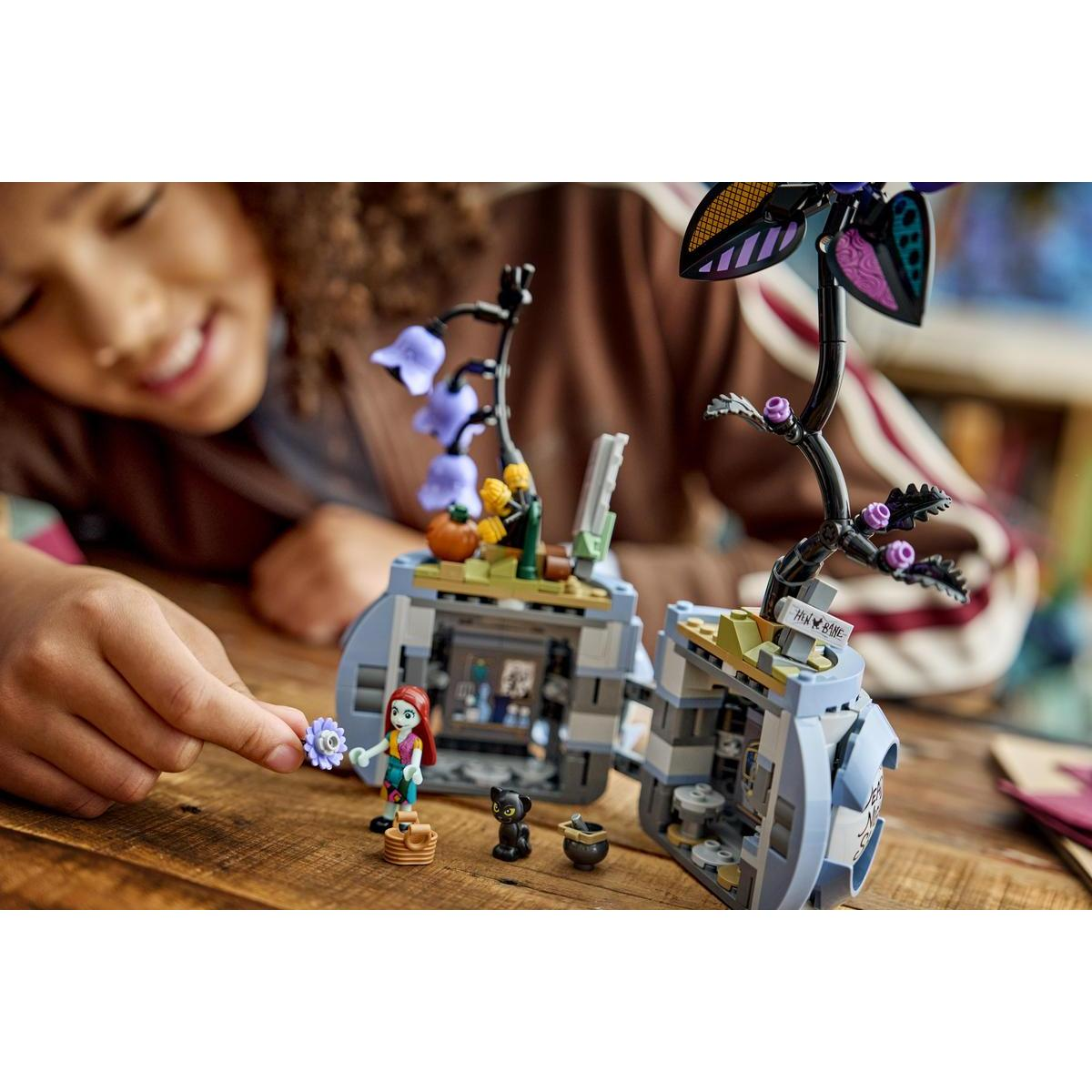 Una ragazza con un fiore blu accanto a un set Lego con un gatto e un calderone.