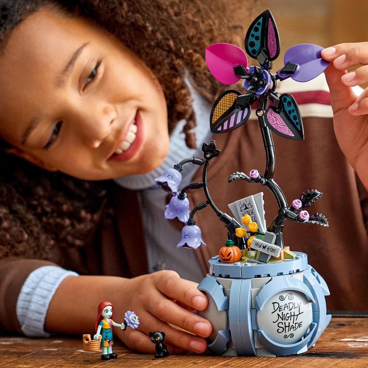 Una ragazza costruisce un fiore LEGO con petali viola e rosa e piccole figure.