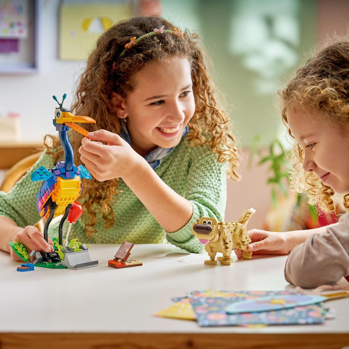 Dos niñas construyen figuras de Lego de un pájaro y un perro en una mesa.