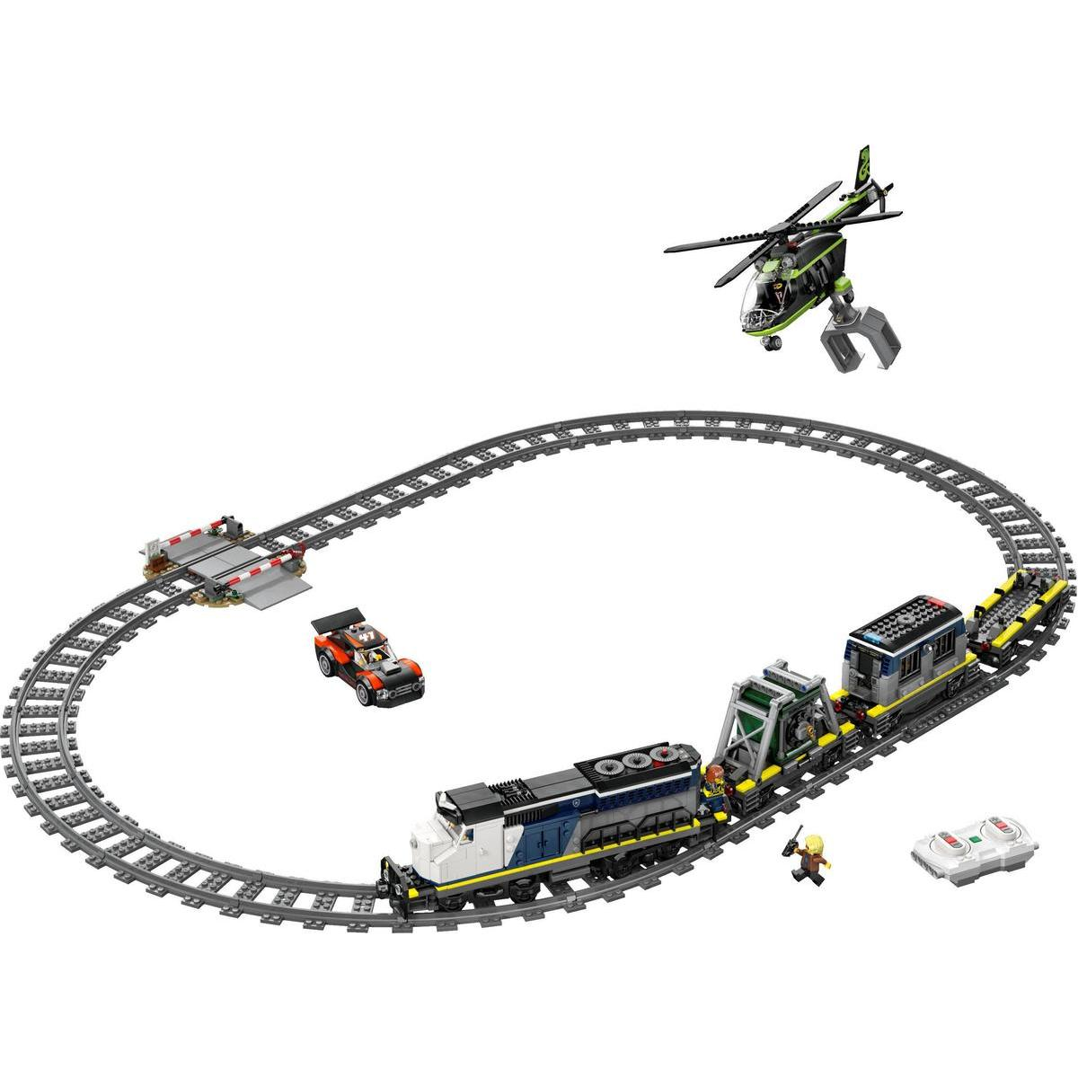 Un tren de juguete con locomotora, vagones, dron, coche y barrera en vías.