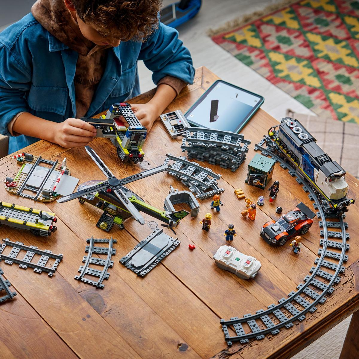 Un niño construye trenes y helicópteros de Lego en una mesa de madera.