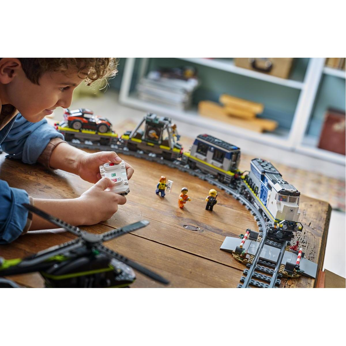 Un niño juega con un tren de juguete, coche y helicóptero en una mesa de madera.