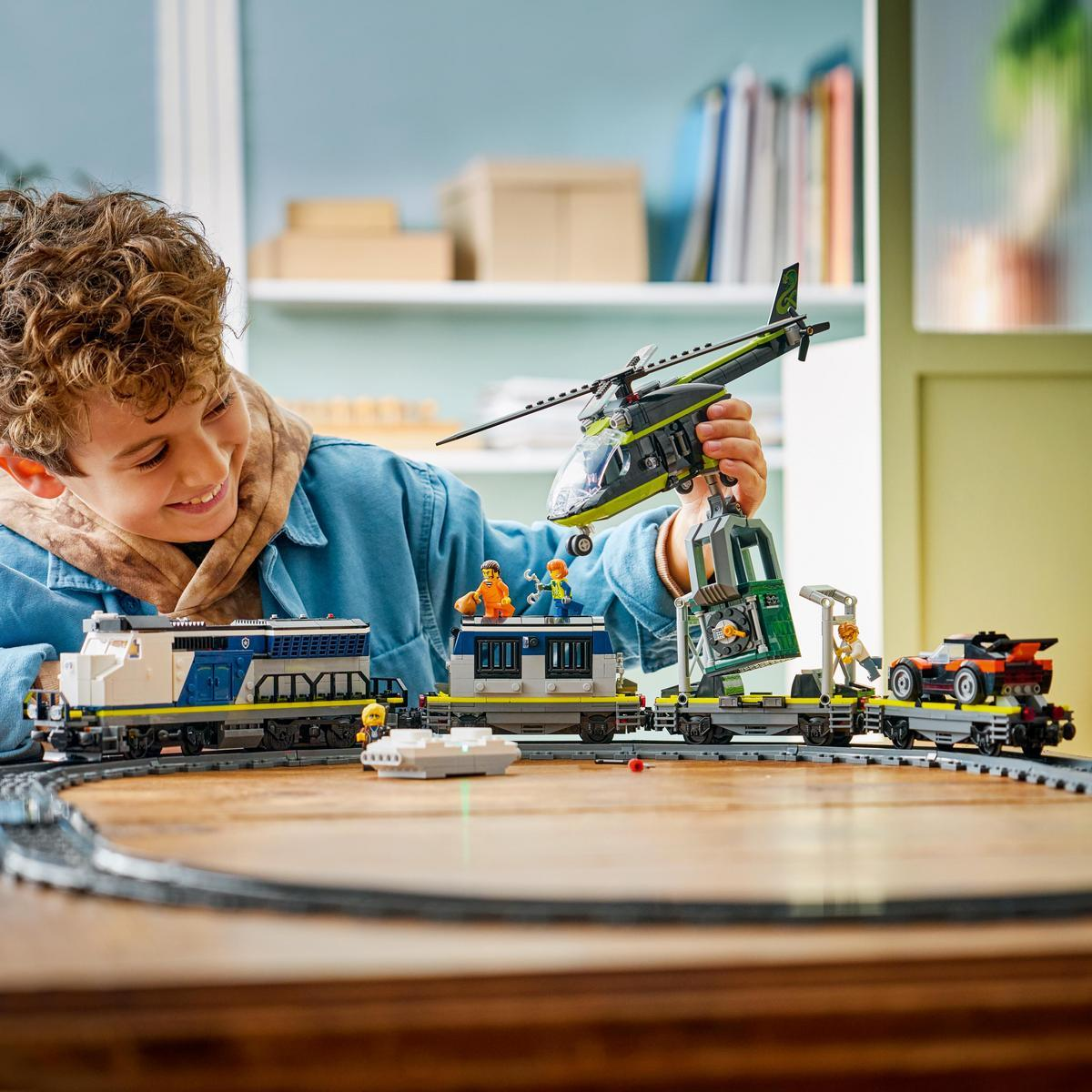 Un niño juega con un tren, helicóptero y coche de Lego en una mesa de madera.